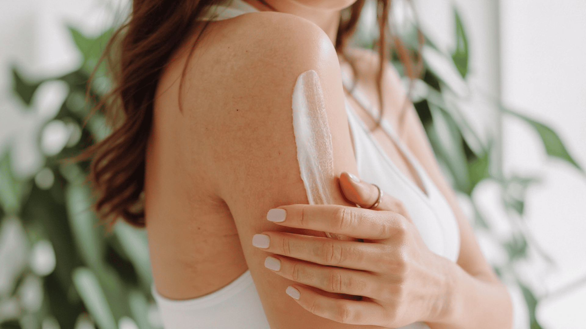 Woman applying moisturizing body lotion to her upper arm as part of a daily skincare routine