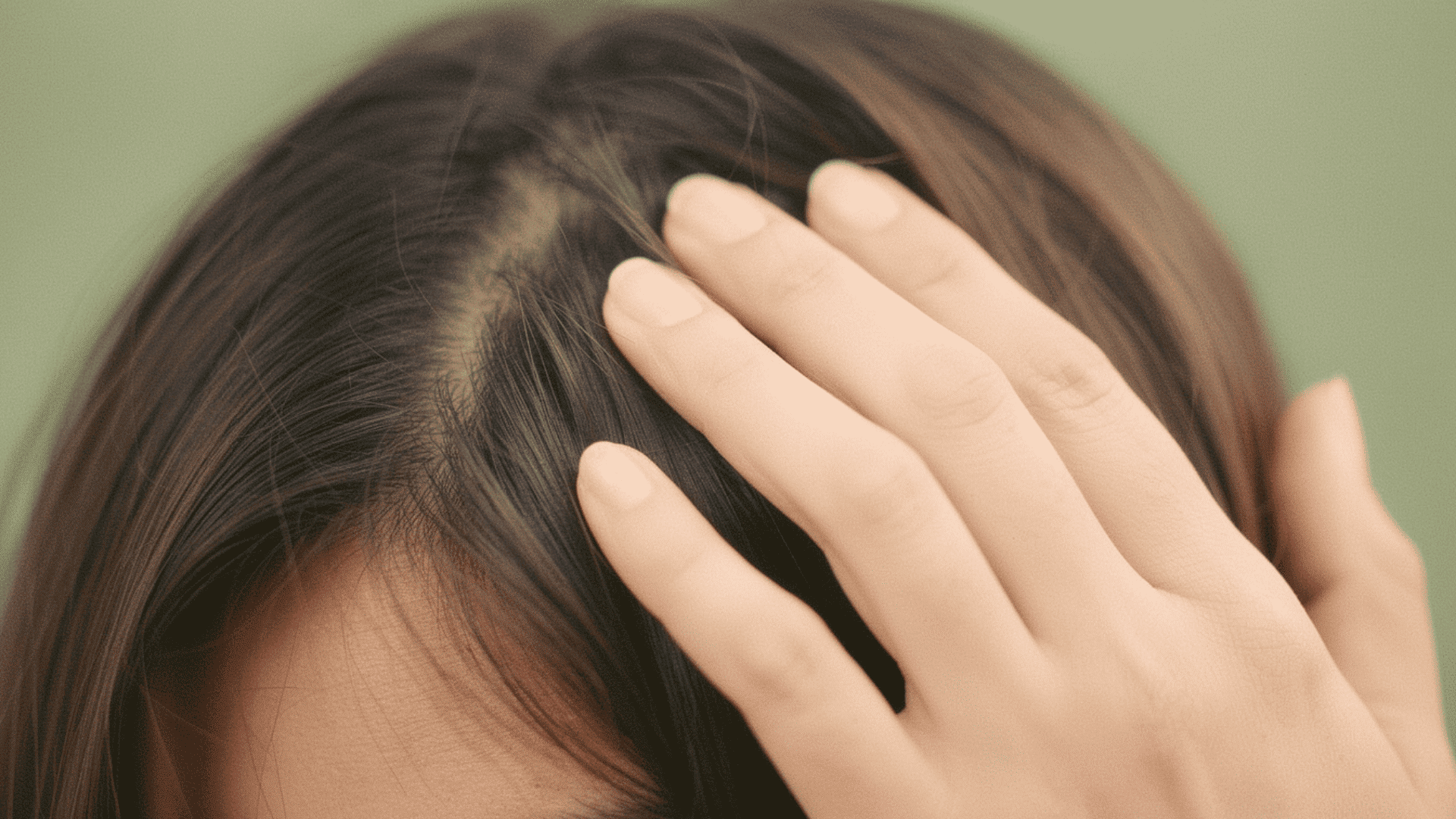 Close-up of a person touching a thinning patch of hair on the top of their scalp