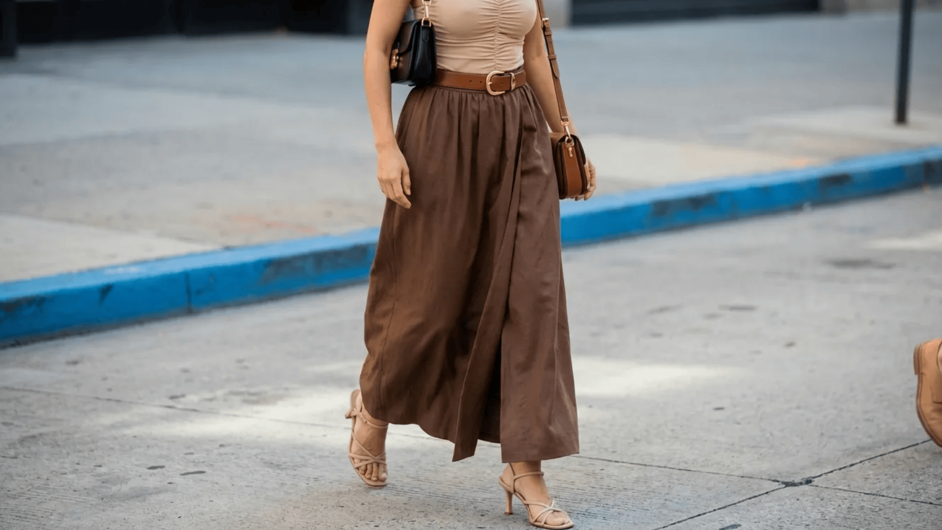 Woman wearing beige top with brown midi skirt, tan heels, and matching brown belt and bag on a street