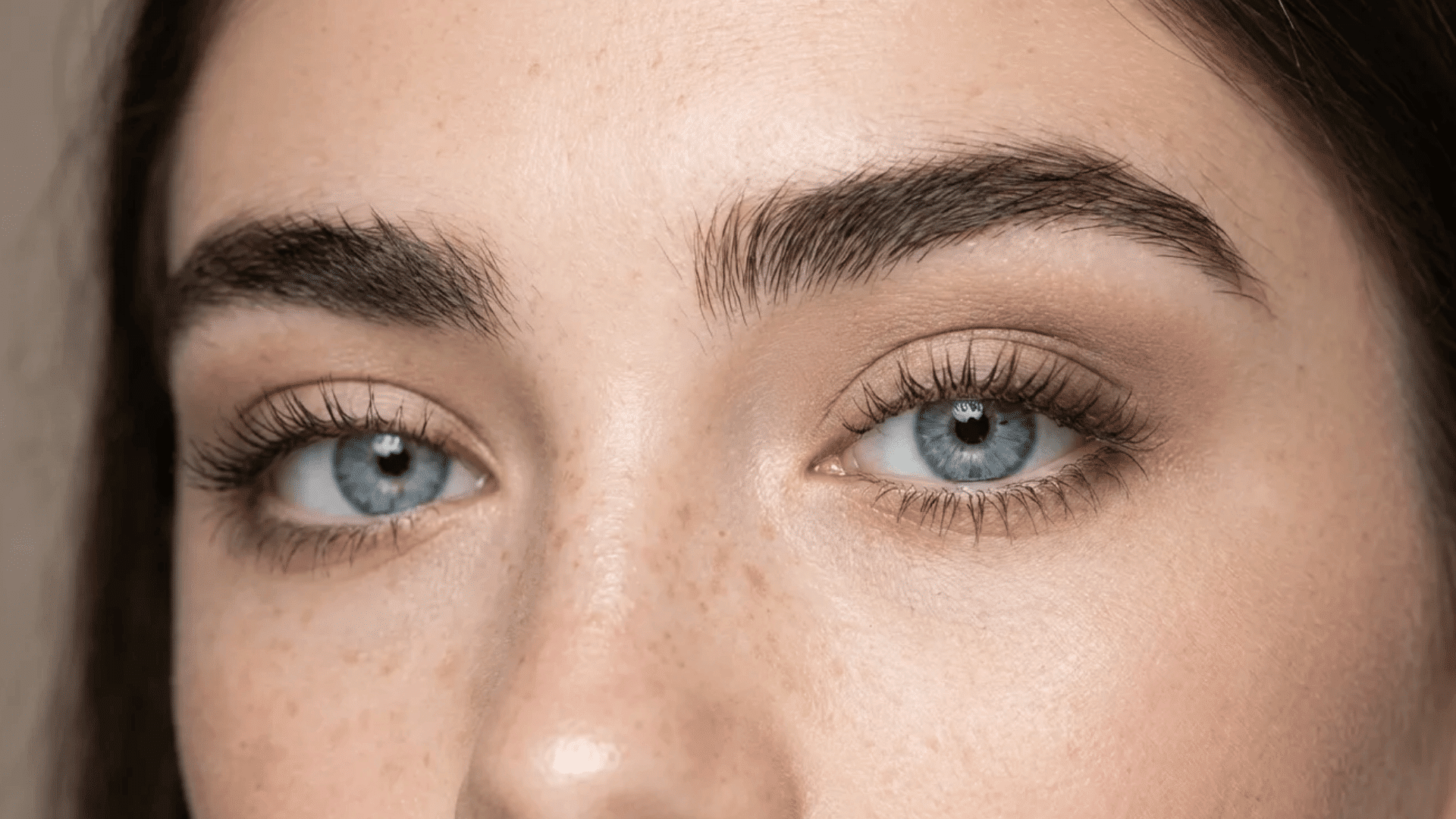 Close-up of blue eyes with natural makeup, long lashes, full brows, and light freckles across the nose and cheeks.