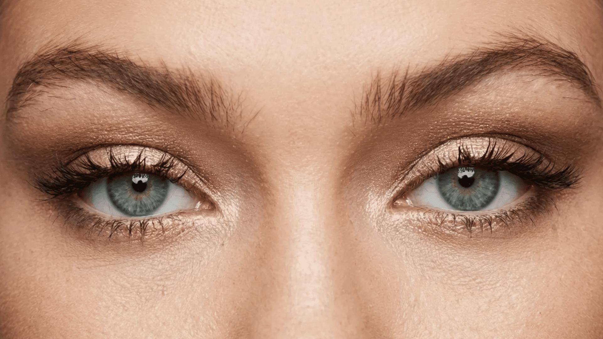 Close-up of green eyes with shimmer eyeshadow, long lashes, and natural, slightly textured eyebrows.