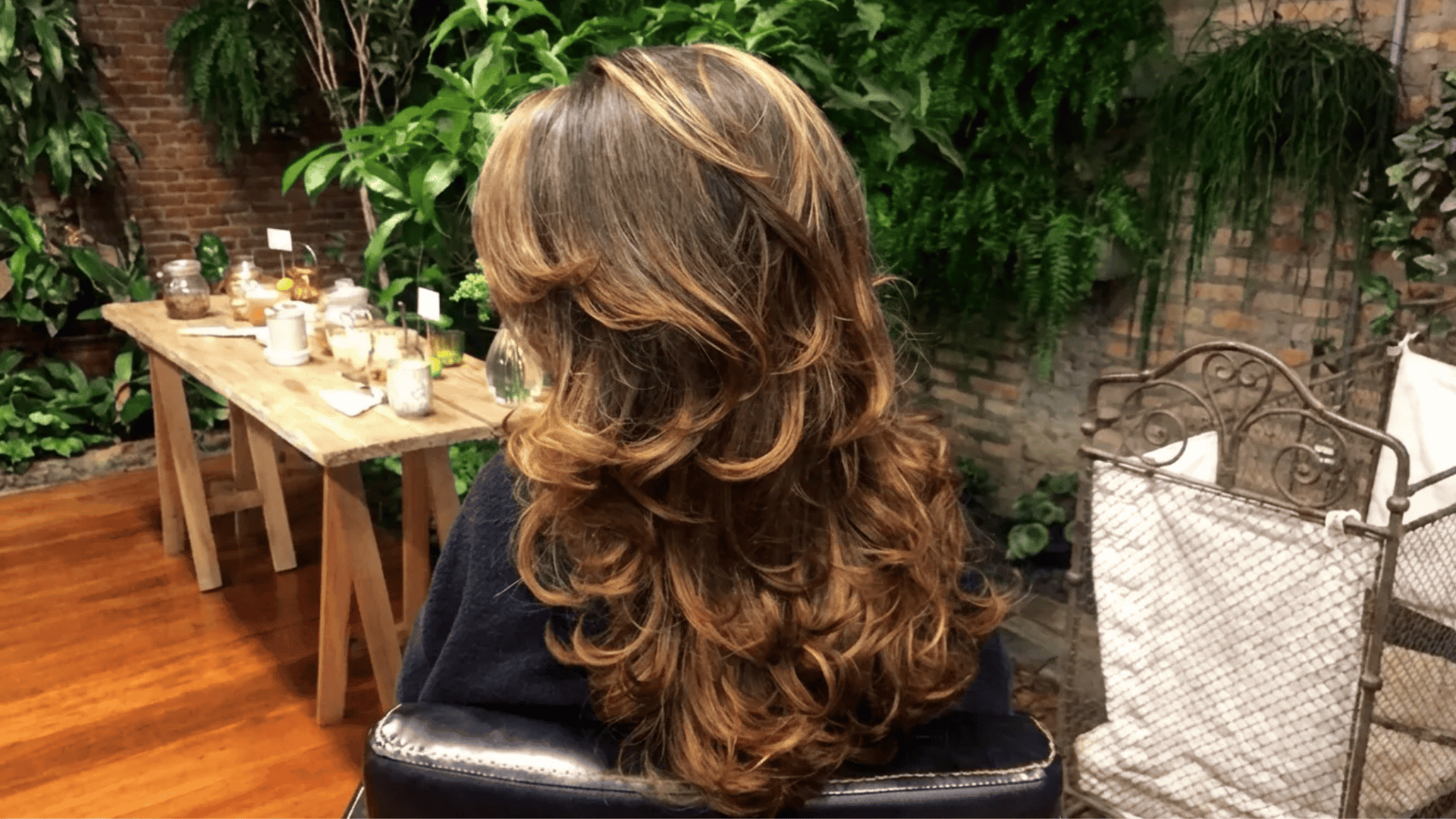 Layered blowout hairstyle with soft curls and warm highlights, styled with volume and smooth finish in a cozy indoor setting