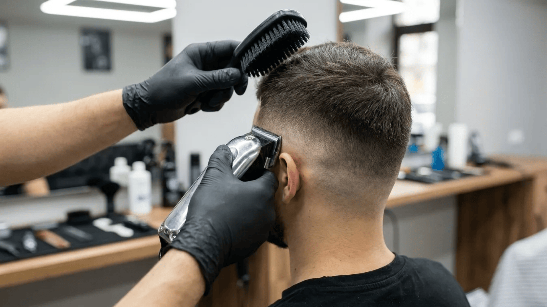 Barber using clippers and brush to blend a short fade haircut on the back and sides of a man’s head