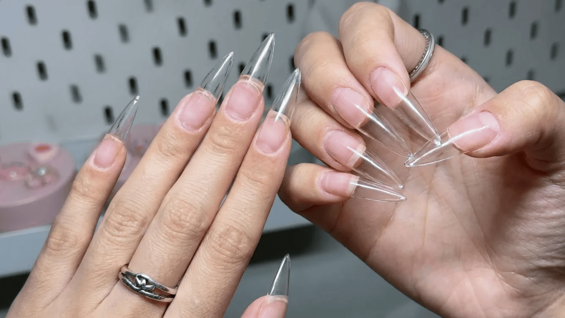 Clear stiletto nail extensions being applied on natural nails, showing transparent tips before polish or design.