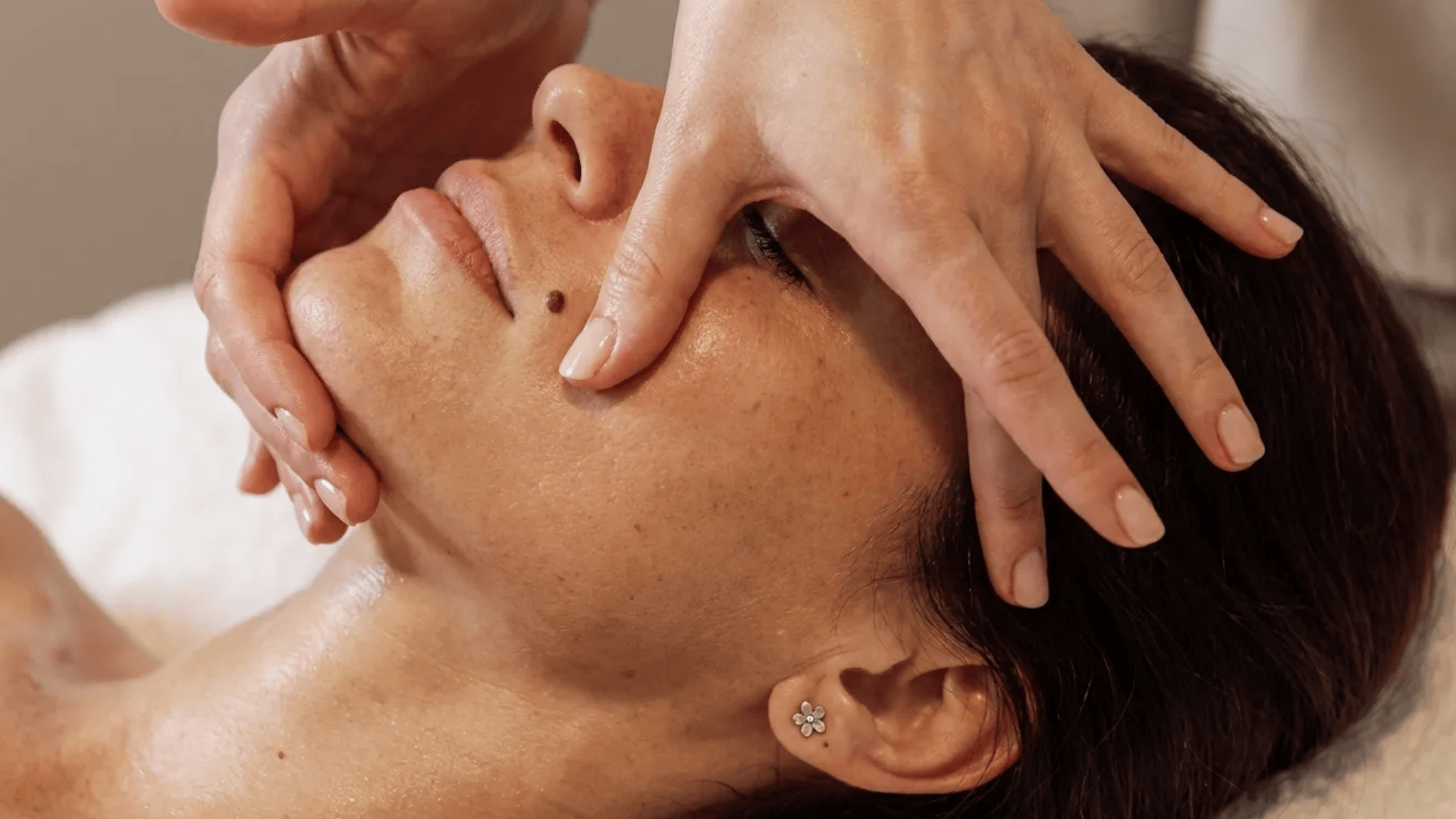 Close-up of a woman receiving a facial massage with hands gently pressing and lifting the skin on her face
