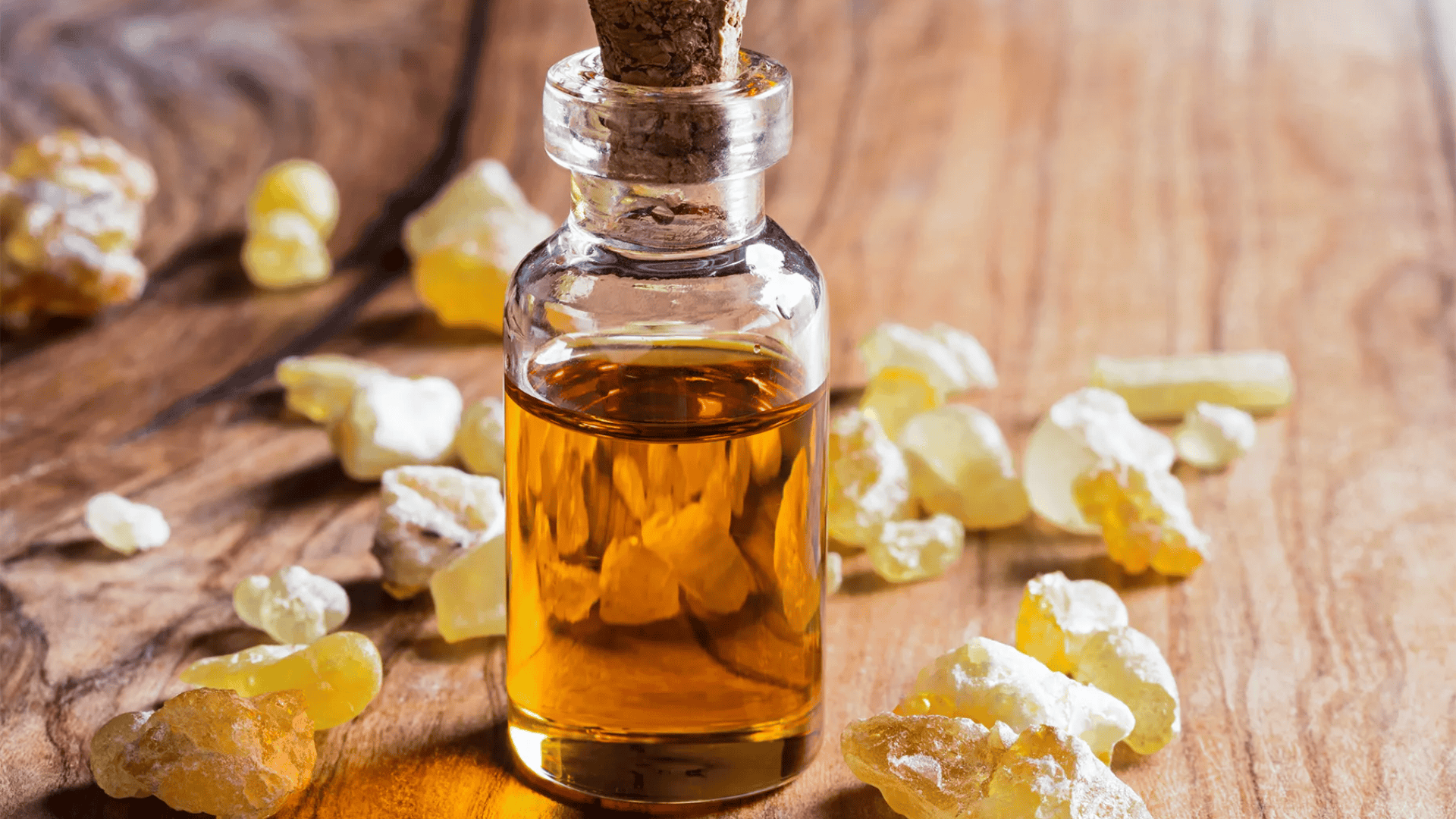 Glass bottle of frankincense oil with resin pieces scattered on a wooden surface