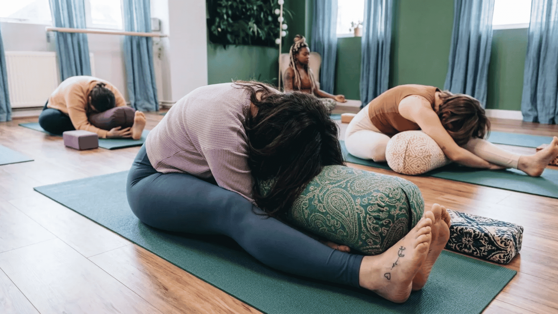 Group of people practicing yin yoga with bolsters in a studio.