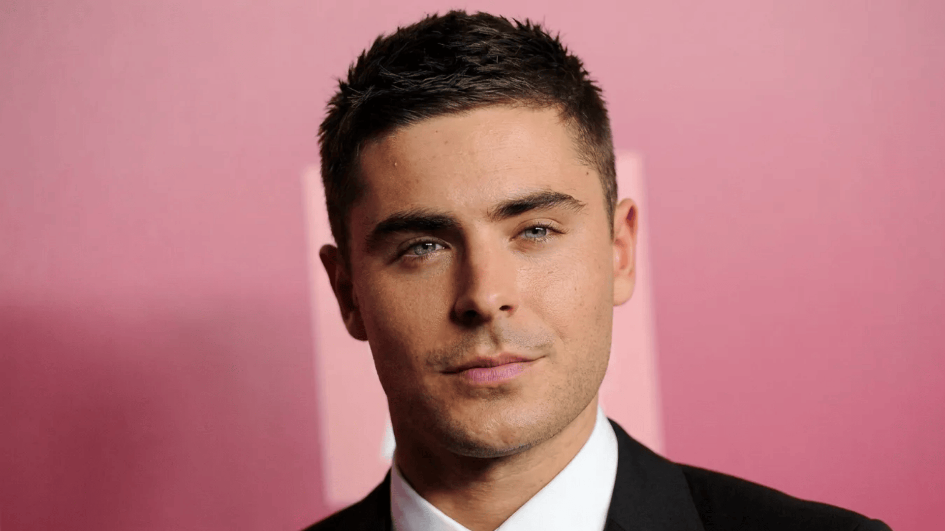Man with short, neat textured haircut and tapered sides, styled clean with a natural finish against a pink background