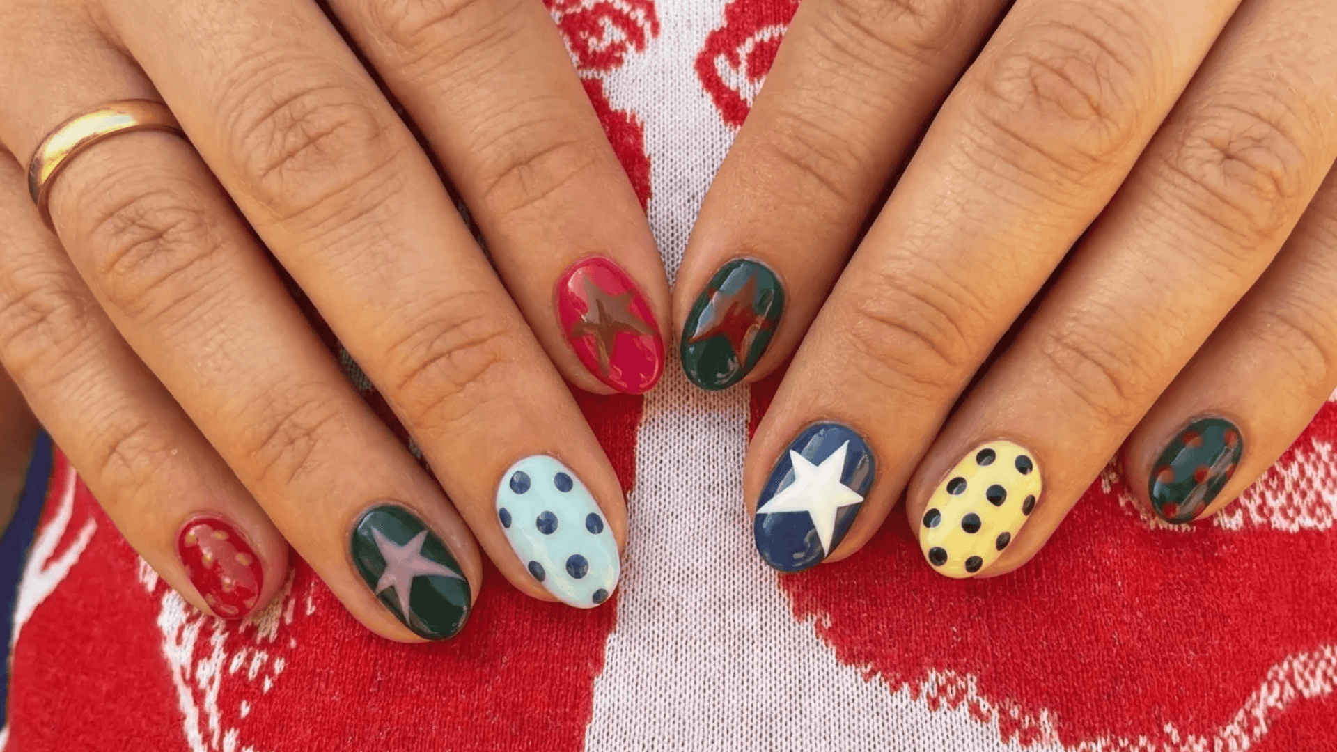 Short oval nails with colorful nail art featuring stars, polka dots, and mixed patterns in red, green, blue, and yellow tones.