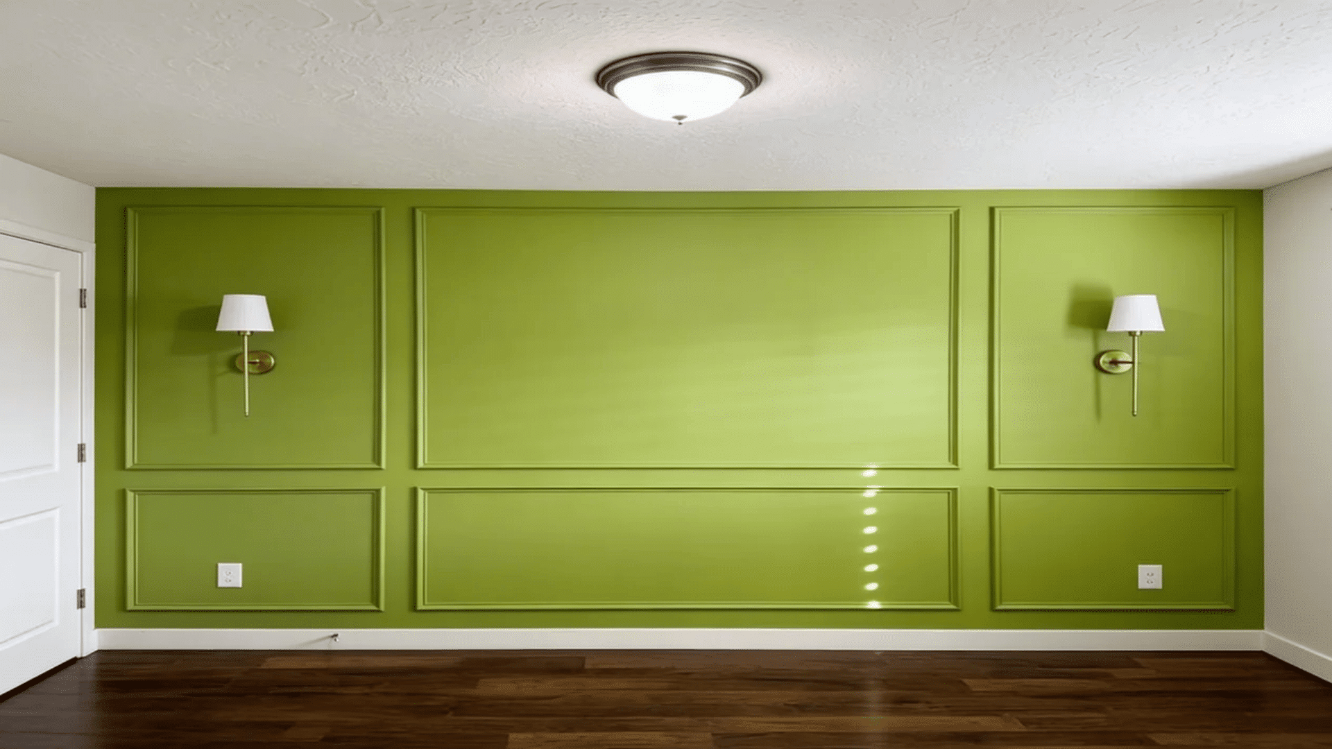 Bright green accent wall with rectangular panel moulding, two wall sconces, dark wood flooring, and a white ceiling light in a minimal interior space.