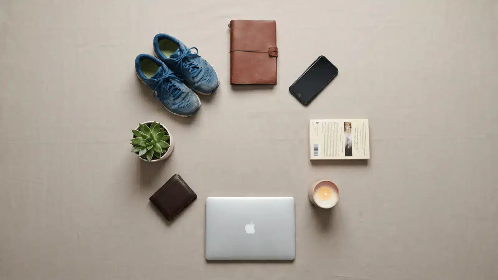 Eight everyday items arranged in a circle including shoes, book, laptop, wallet, and plant