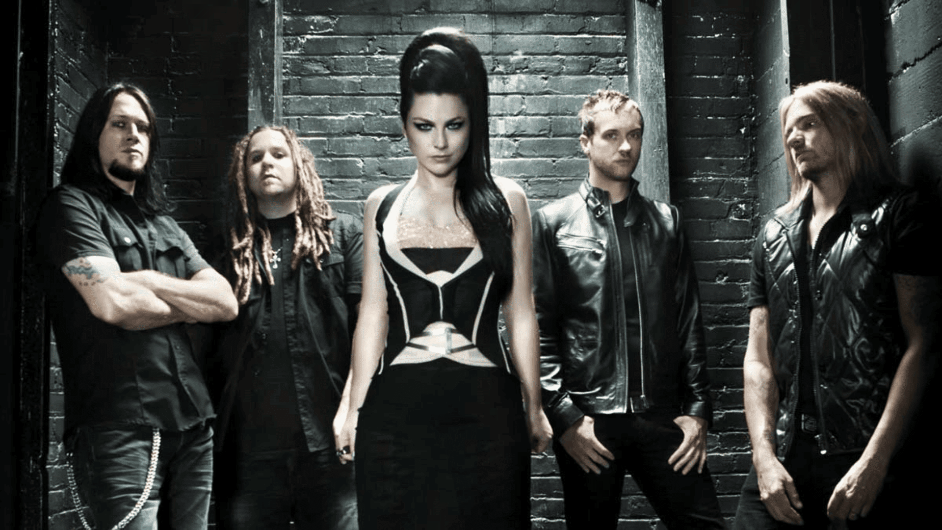 Evanescence band members in dark outfits standing against a brick wall with moody lighting and gothic-inspired styling
