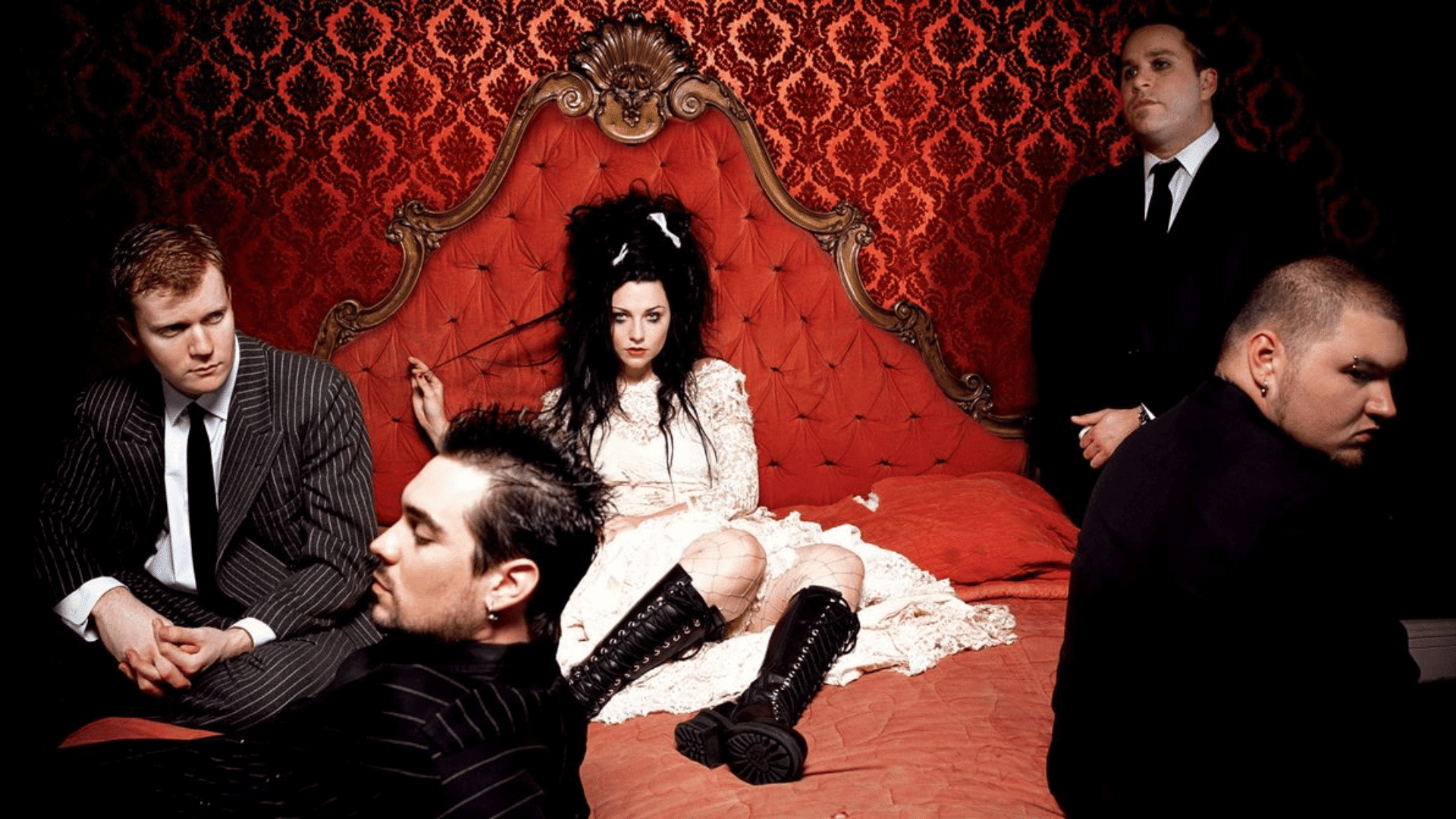 Evanescence band posed in a gothic-style room with red patterned walls and vintage bed, featuring dramatic fashion and dark aesthetic styling