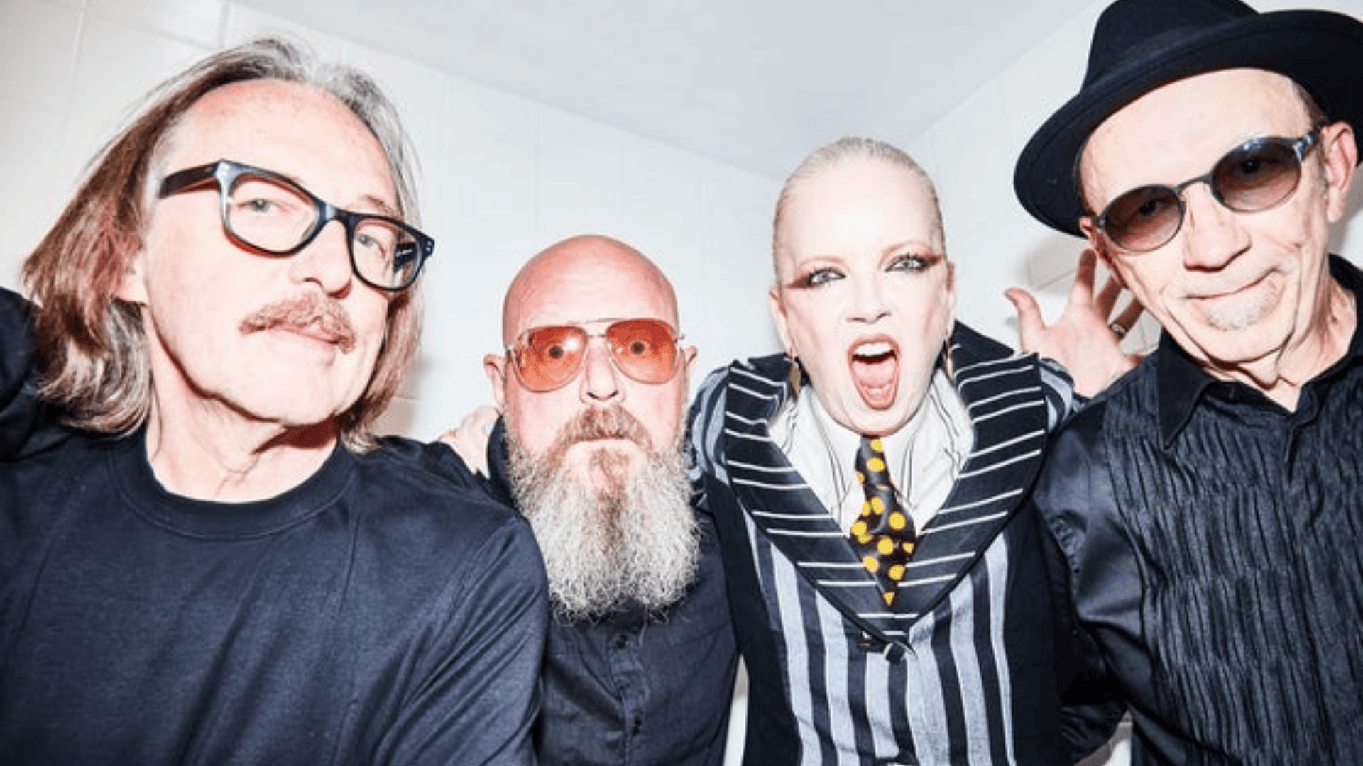 Shirley Manson posing with band members in a striped suit and tie, making an expressive face while others stand beside her