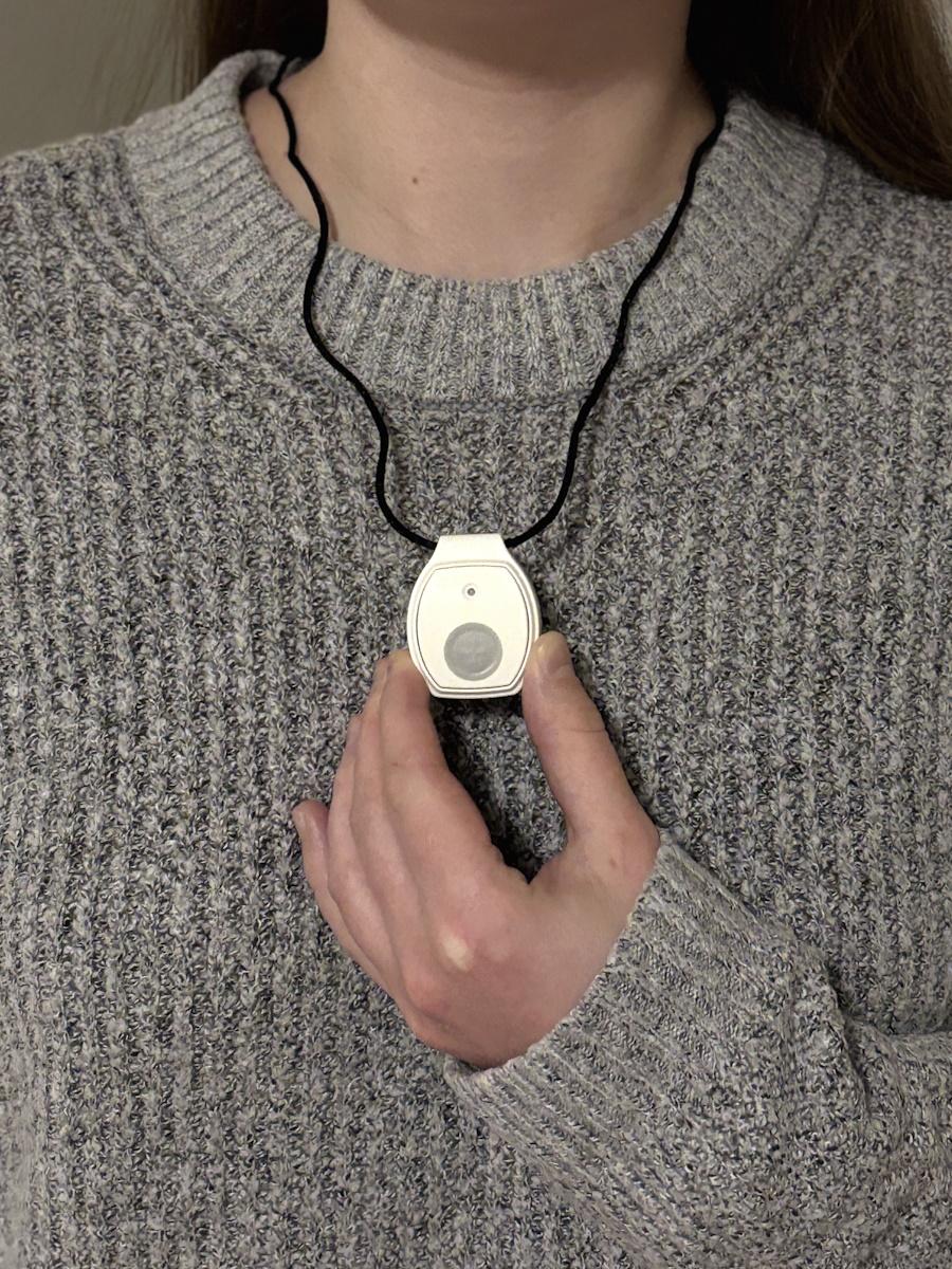 A medical alert pendant worn over a grey sweater