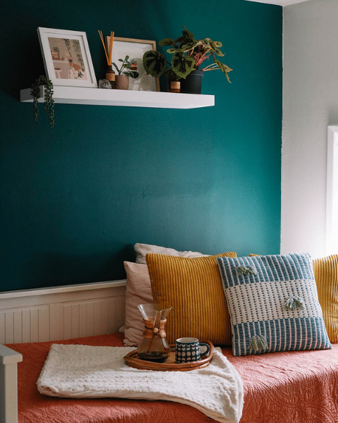 A cozy corner with teal walls, a bed with colorful pillows, and a tray with a coffee mug and coffee maker.