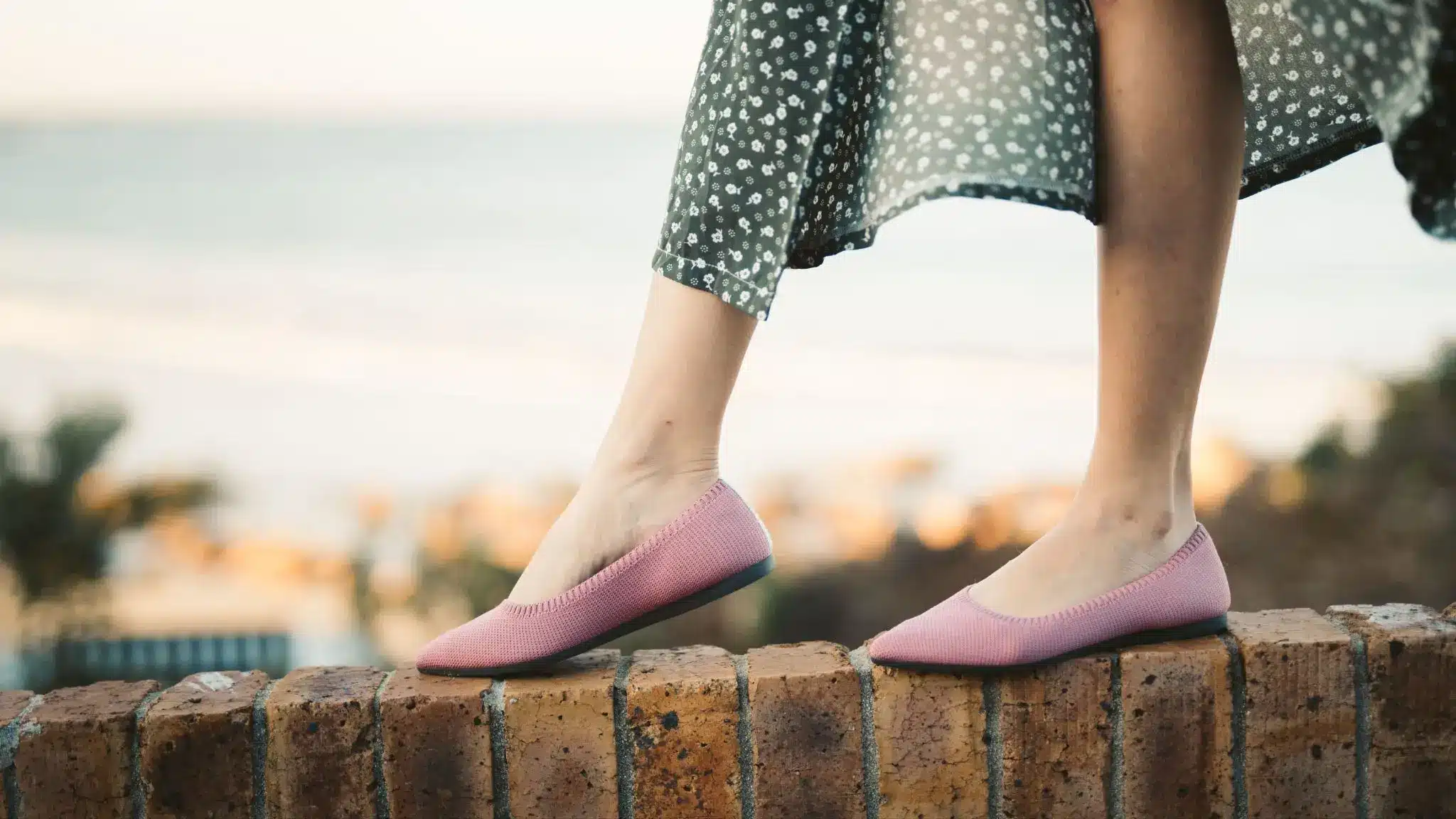 Pink ballet flats on brick wall with ocean view background