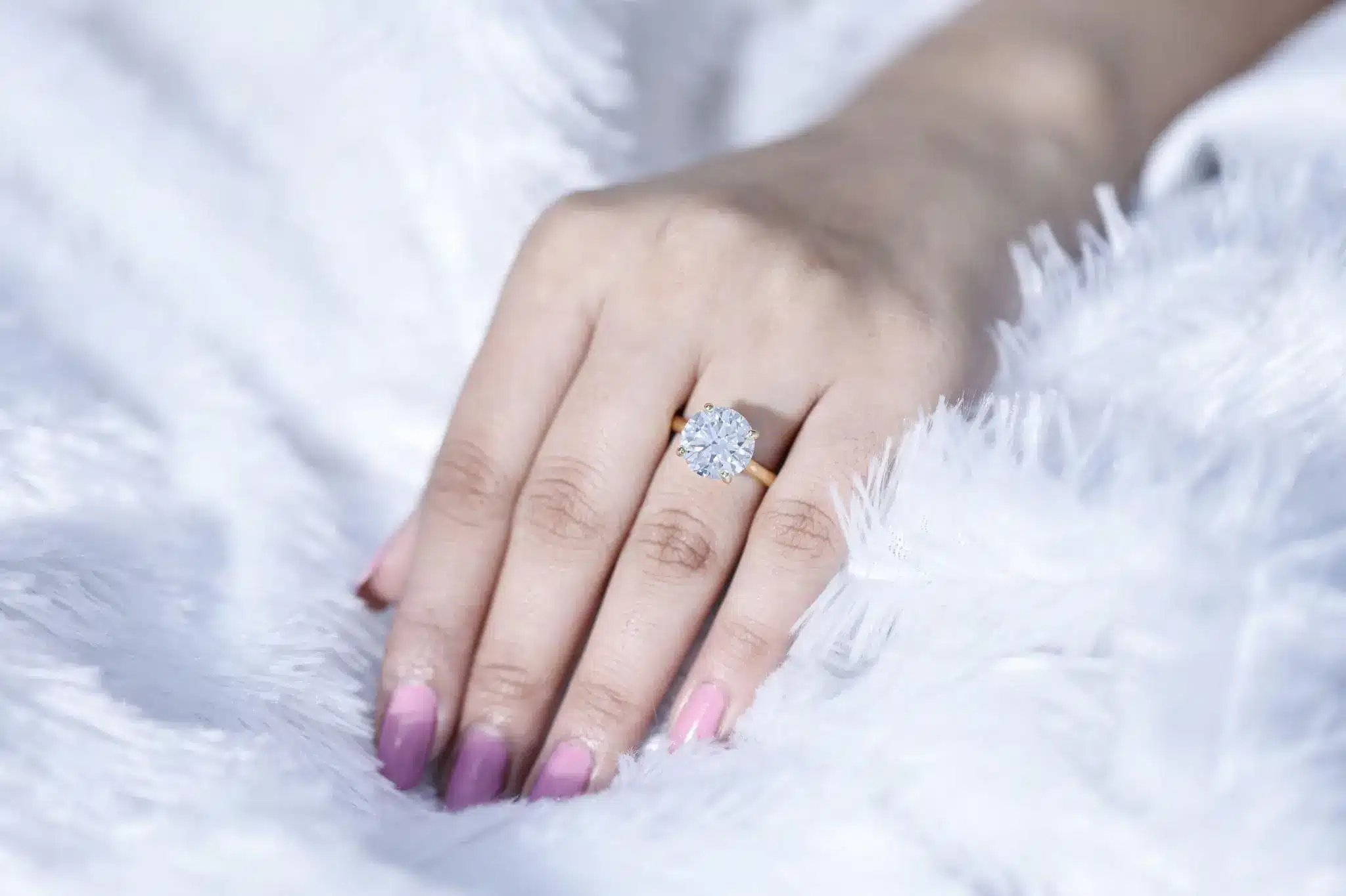 Close-up of a hand with a diamond engagement ring on a fluffy white surface