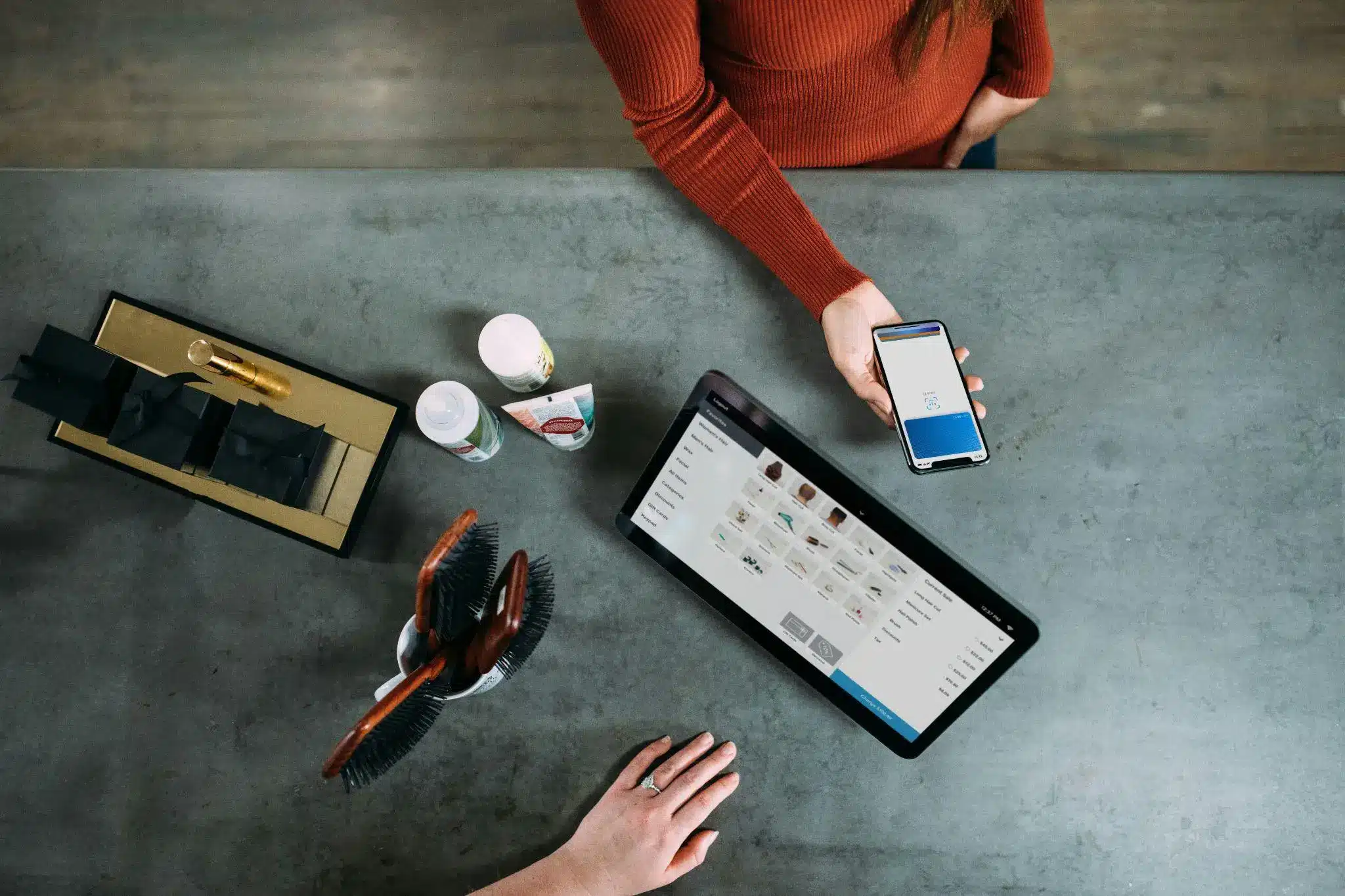 Woman paying with smartphone at salon counter with hairbrushes and tablet display