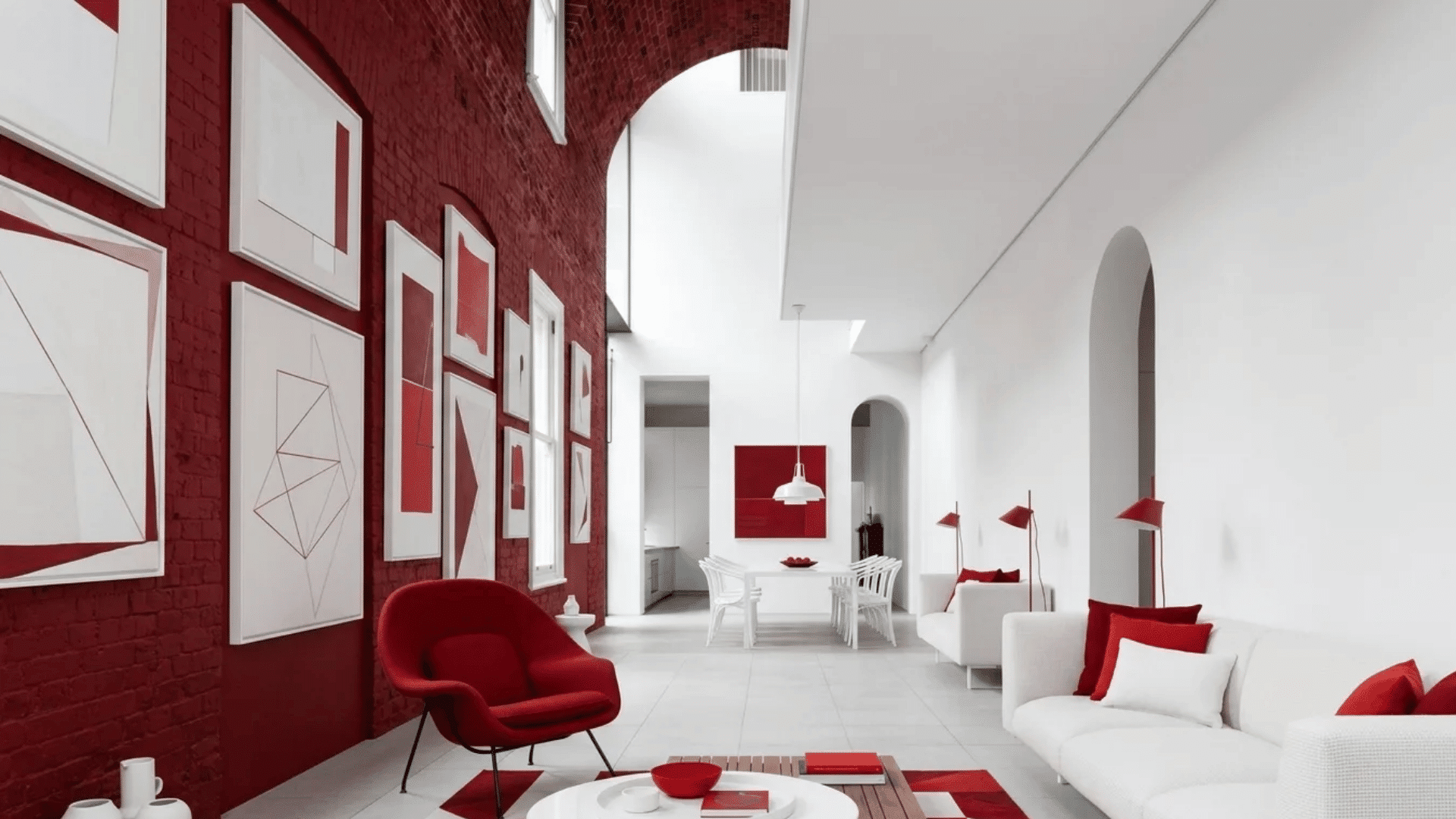 Modern white and red living room with bold contrast, framed wall art, red accent chair, white sofa, and tall arched ceiling.