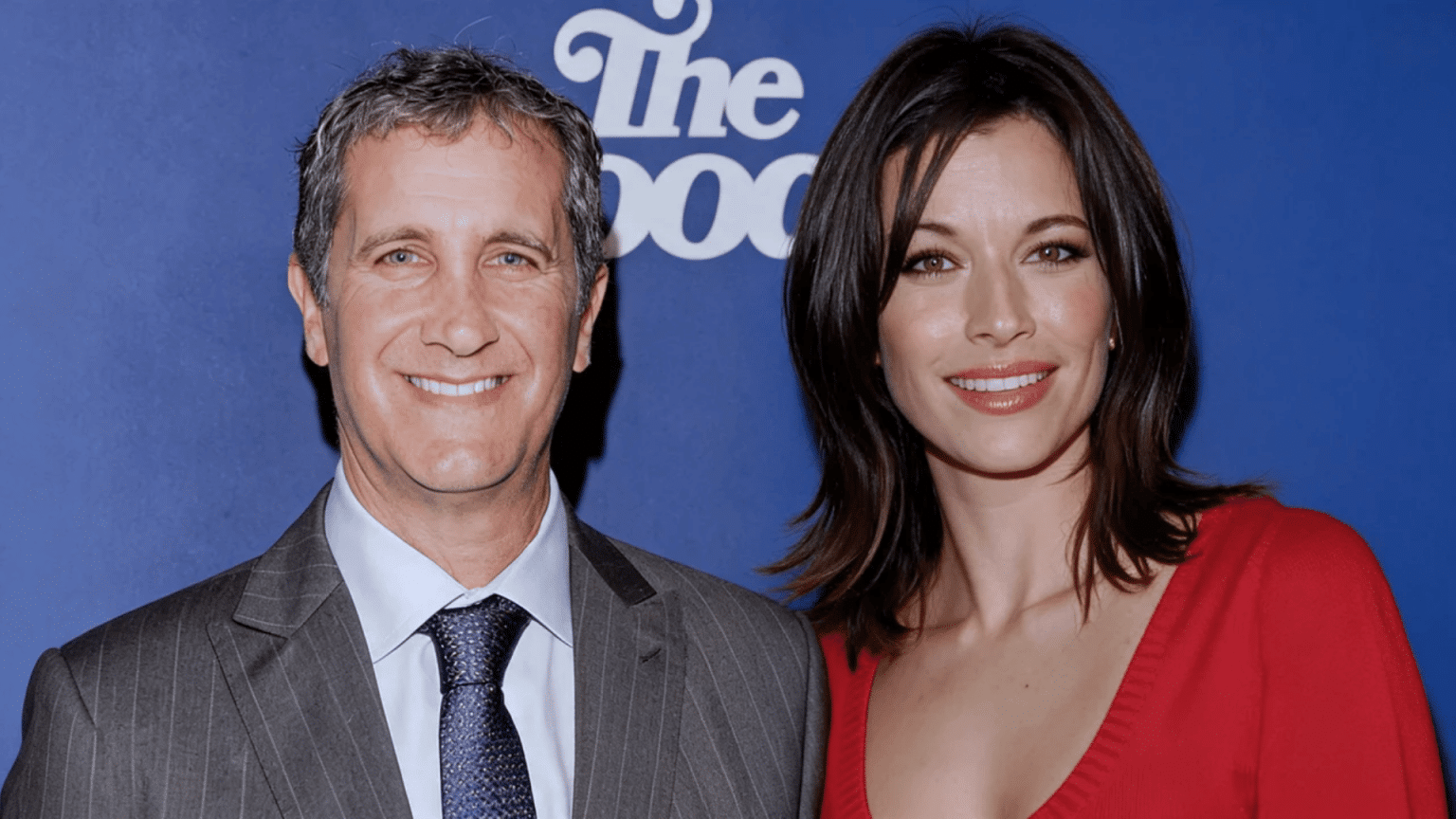Brooke Langton posing with a man at an event against a blue backdrop.