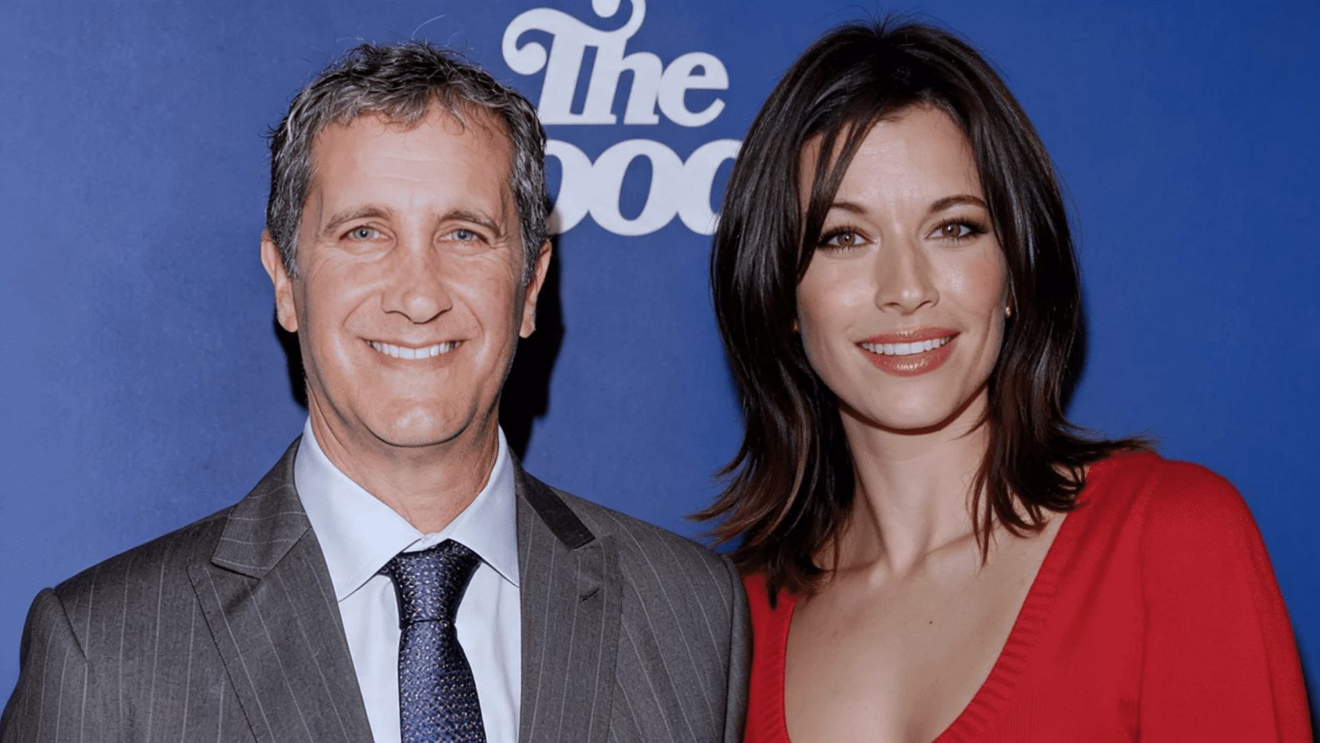 Brooke Langton posing with a man at an event against a blue backdrop.
