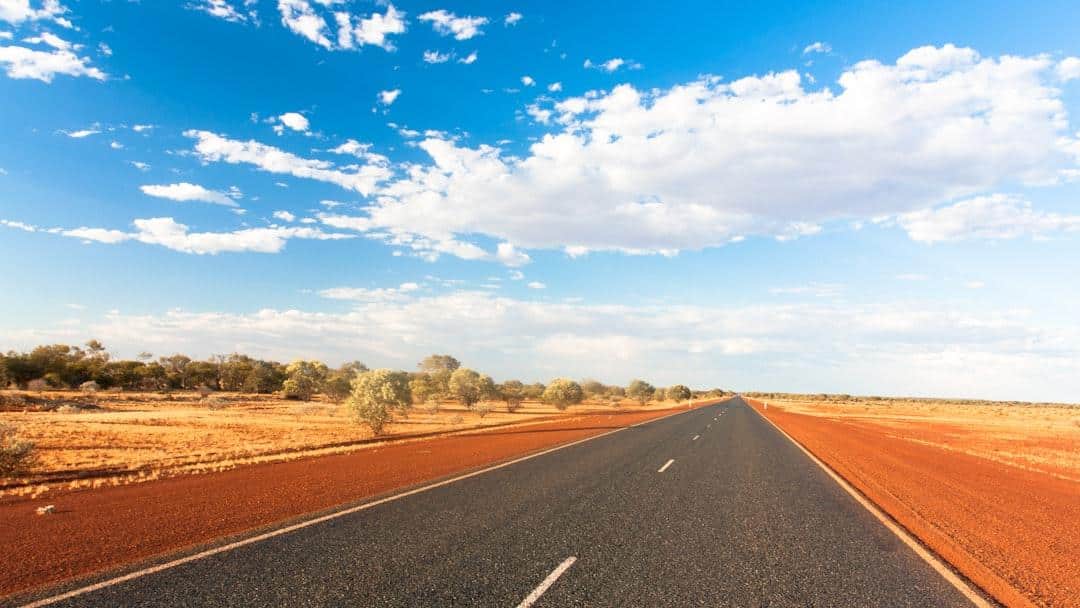 An open road stretching through the Australian outback under a blue sky