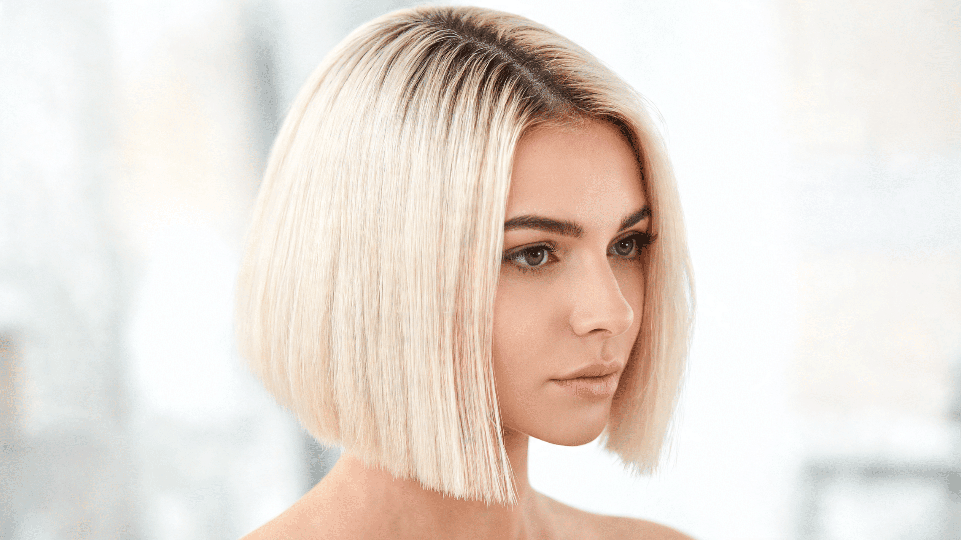 Woman with a platinum blonde bob sew-in hairstyle featuring dark roots and a structured short cut.
