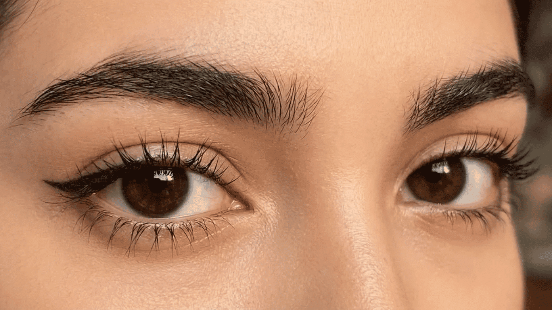 Close-up brown eyes with long eyelashes, defined eyebrows, and natural skin texture visible