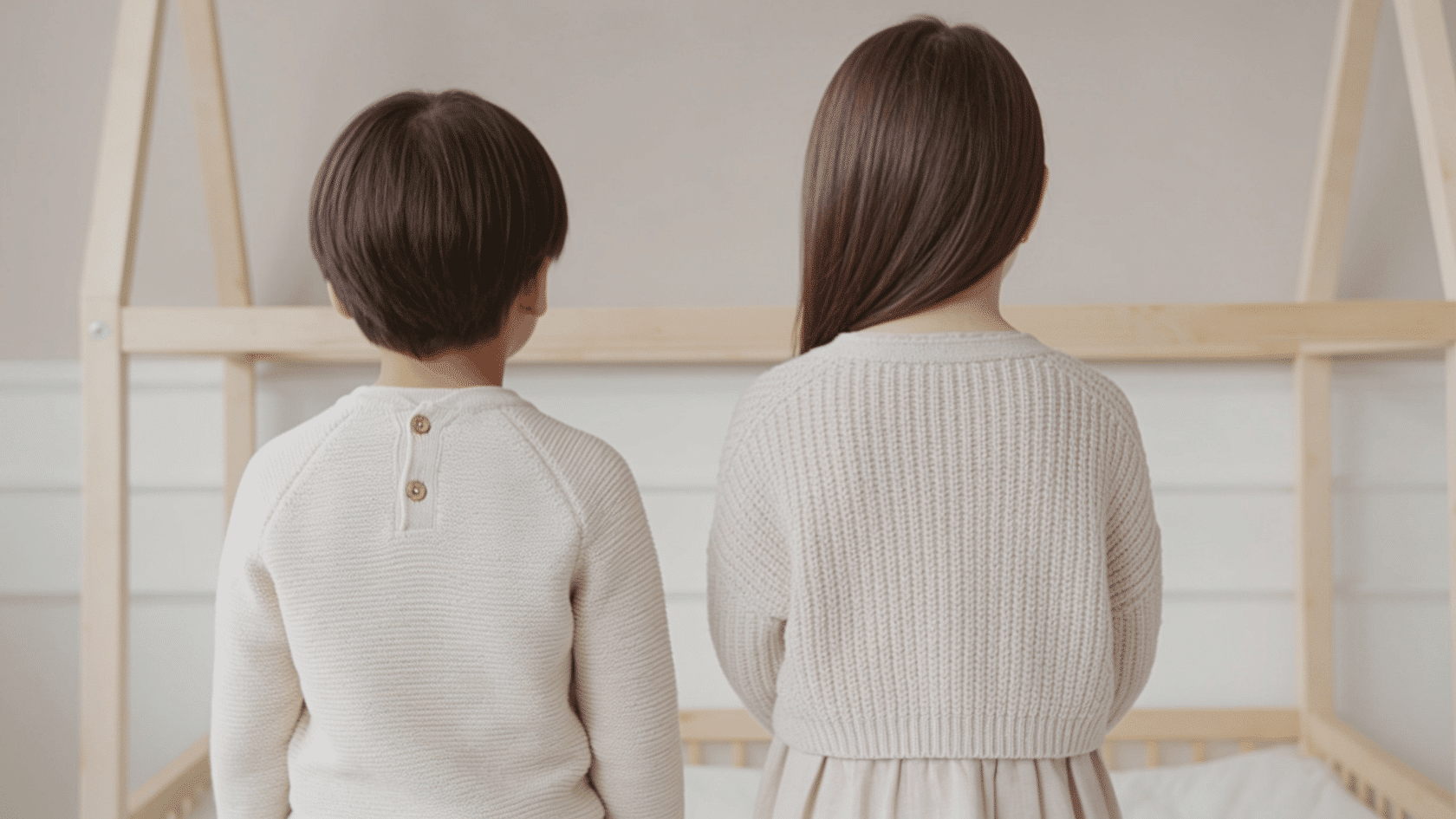 Two children wearing coordinated neutral outfits in a simple indoor newborn photoshoot setting