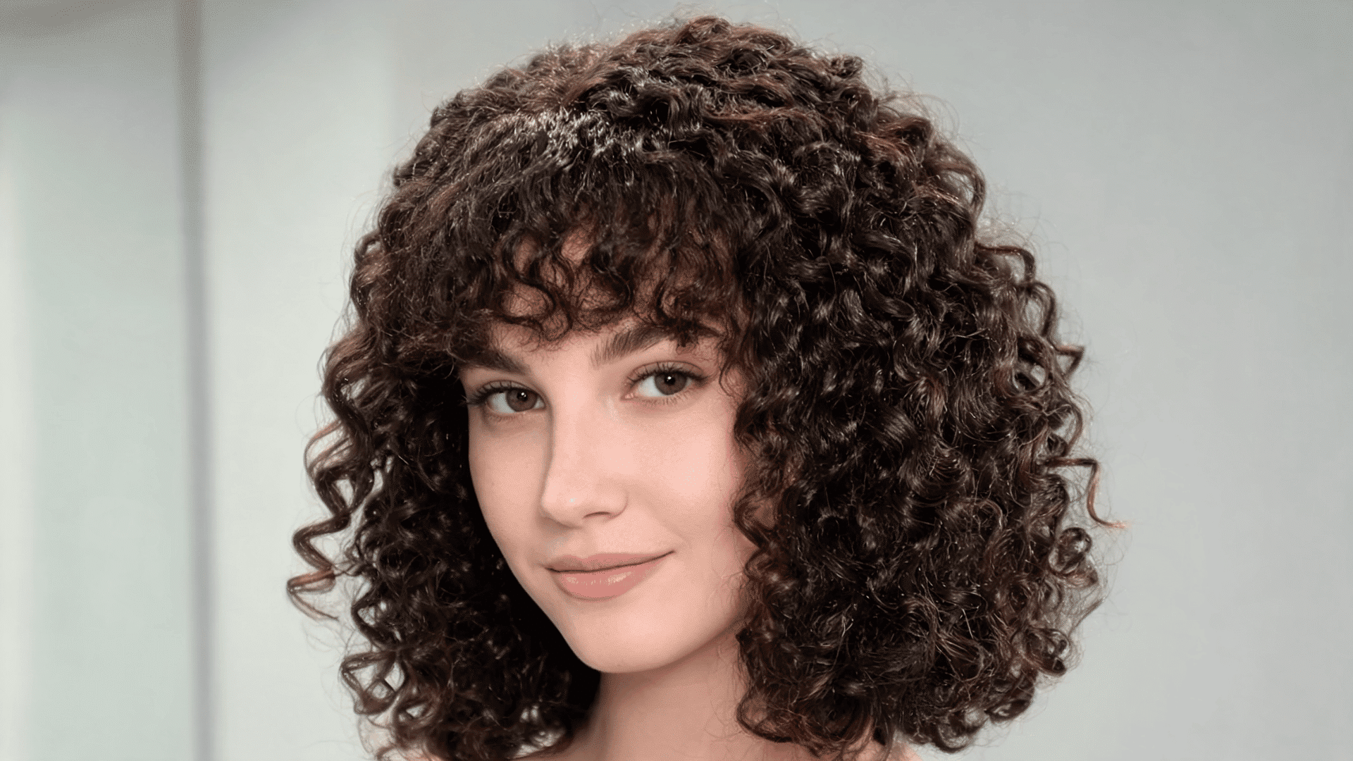 Woman with a kinky curly sew-in hairstyle featuring textured curls and face-framing bangs.