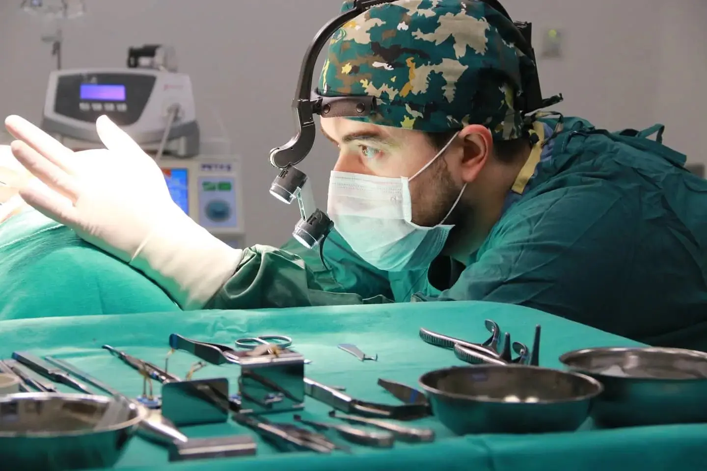 Surgeon in operating room wearing surgical mask and headlamp with instruments on tray