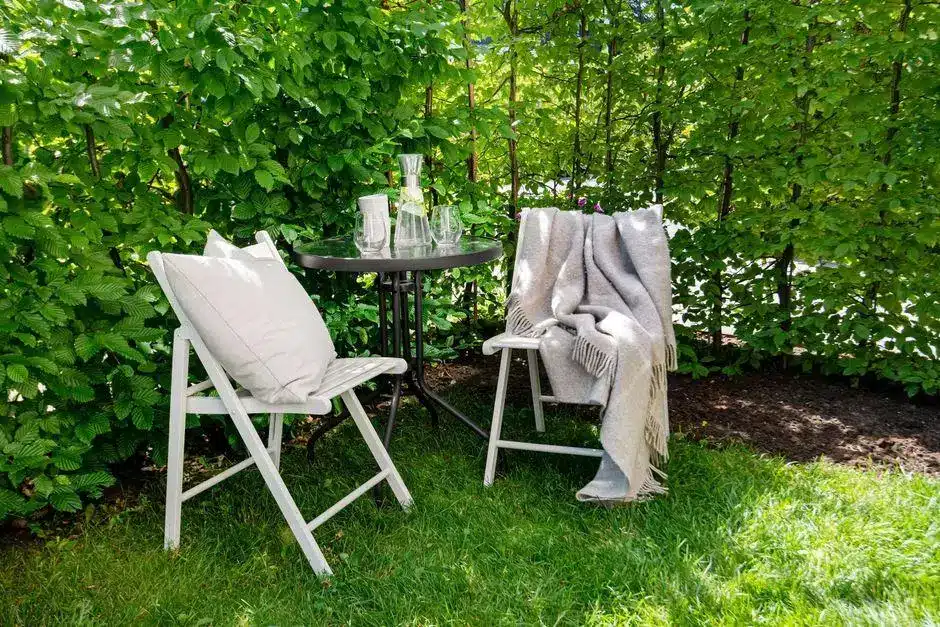 Two chairs with cushion and throw blanket beside small table in lush garden setting