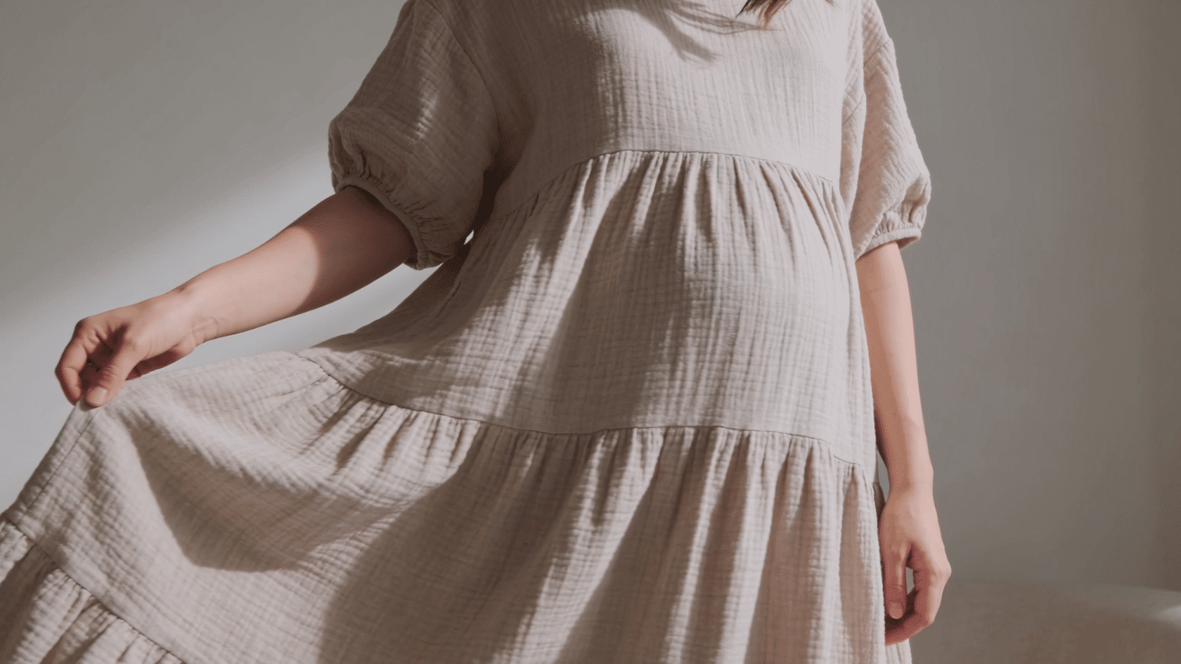 Woman wearing a loose flowing dress in a simple indoor setting with soft natural light