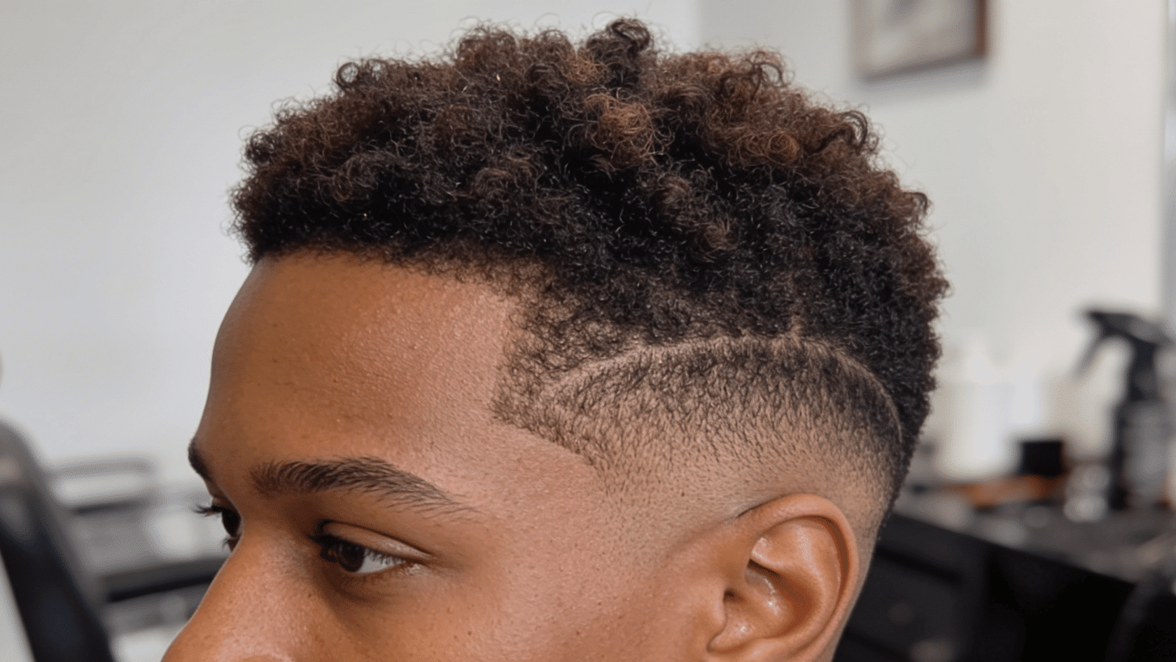 Close-up side profile of a man with short curly fade haircut in a barbershop