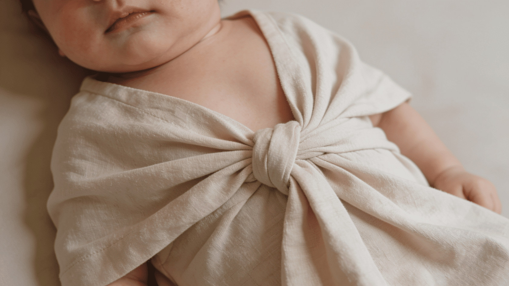 Baby wearing a knotted gown in a soft indoor setting with visible fabric folds