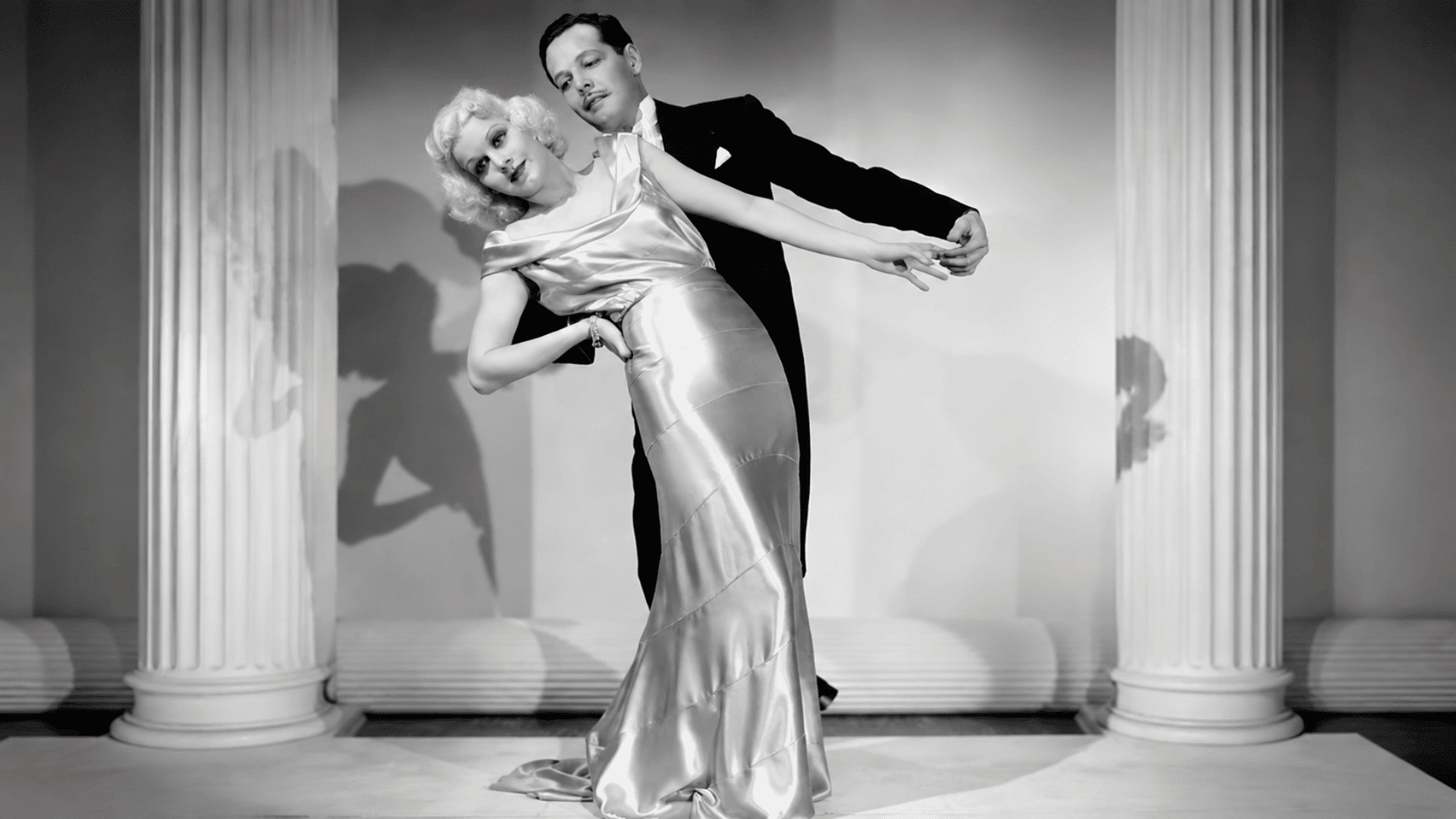 1930s formalwear couple in a dance pose between tall columns.