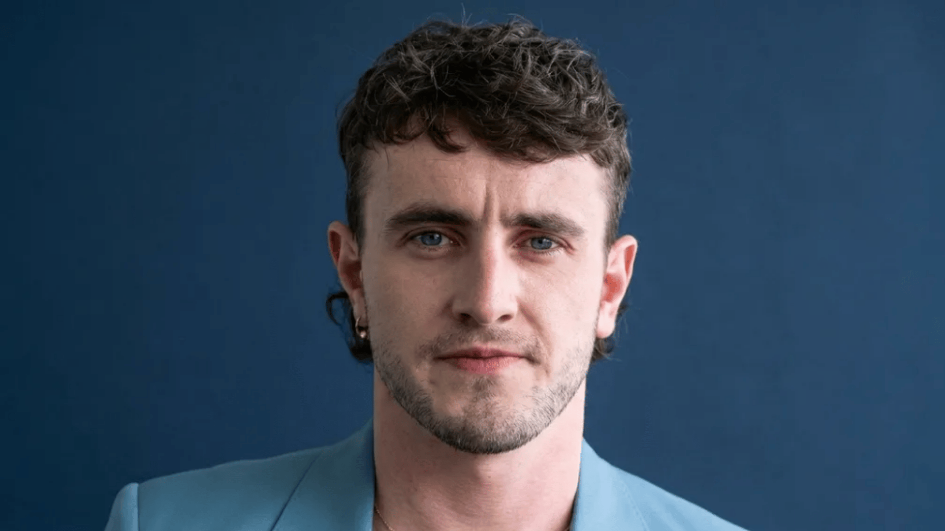 Man with short mullet haircut featuring short textured top, faded sides, and slightly longer back against a blue background.
