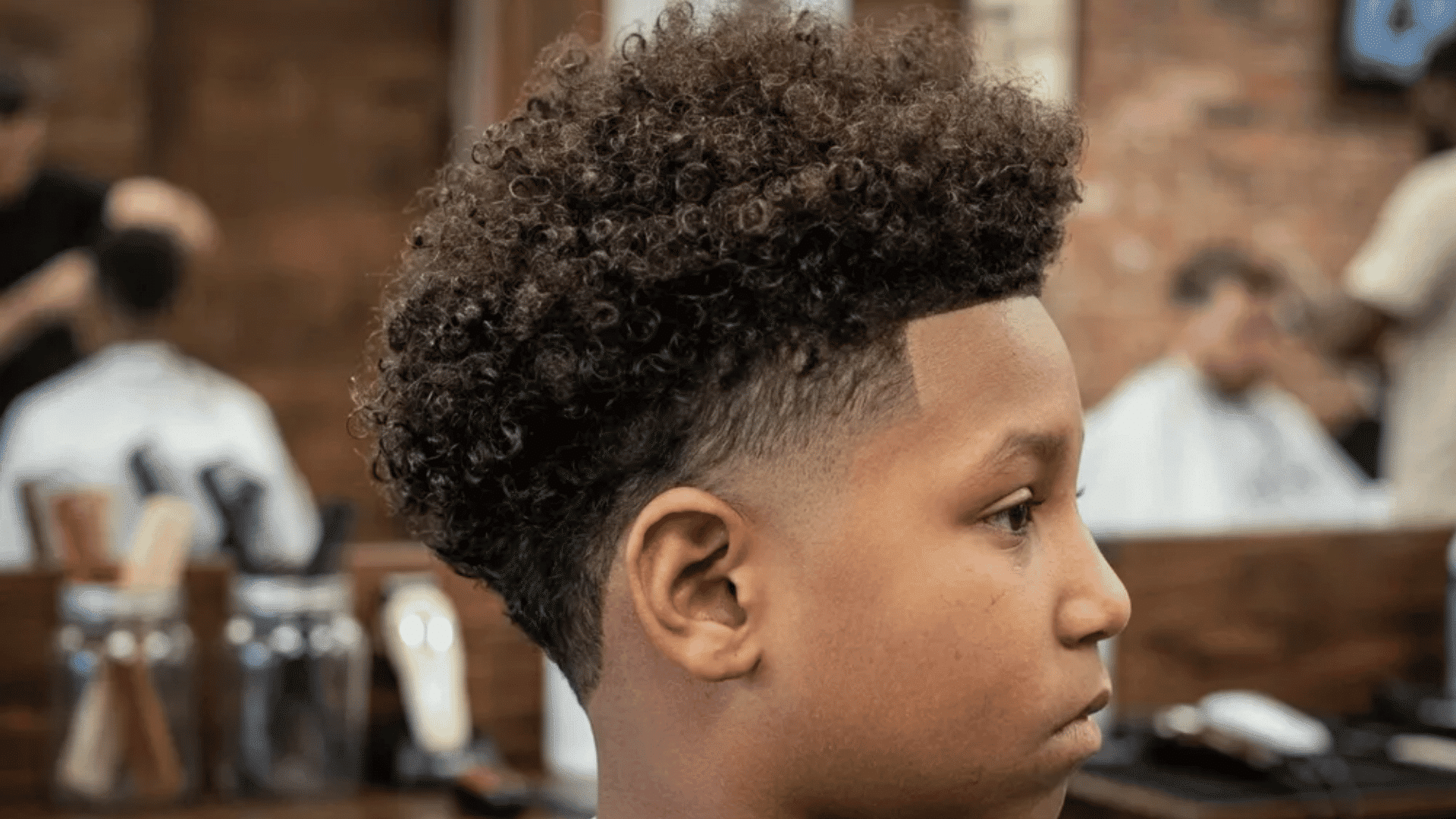 Mixed boys haircuts curly fade style on a boy with tight curls and low skin fade in a barber shop