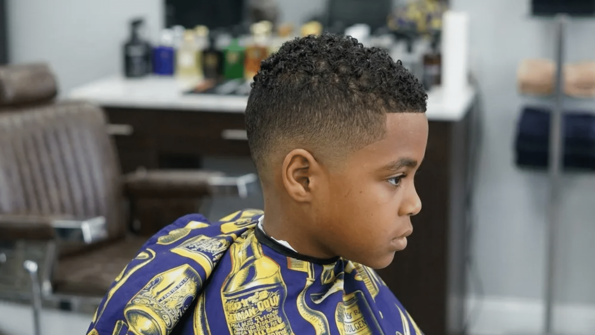 Mixed boys haircuts curly top with high taper fade and sharp lineup on young boy in barber shop side profile view