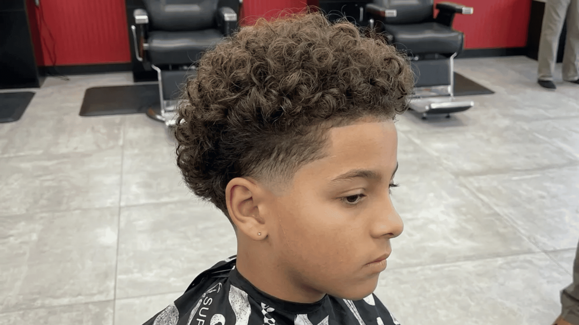 Mixed boys haircuts curly top with mid fade on young boy in barber shop with defined curls and clean faded sides seen in side profile