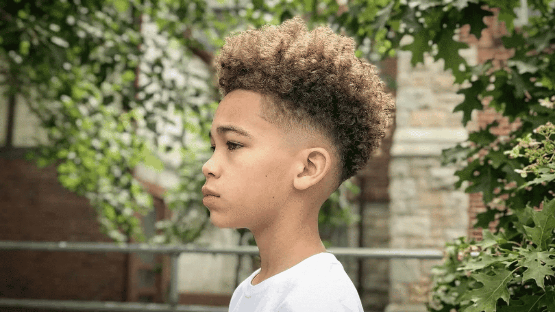 Mixed boys haircuts high taper curly fade style on boy with natural curls and clean taper seen in side profile outdoors