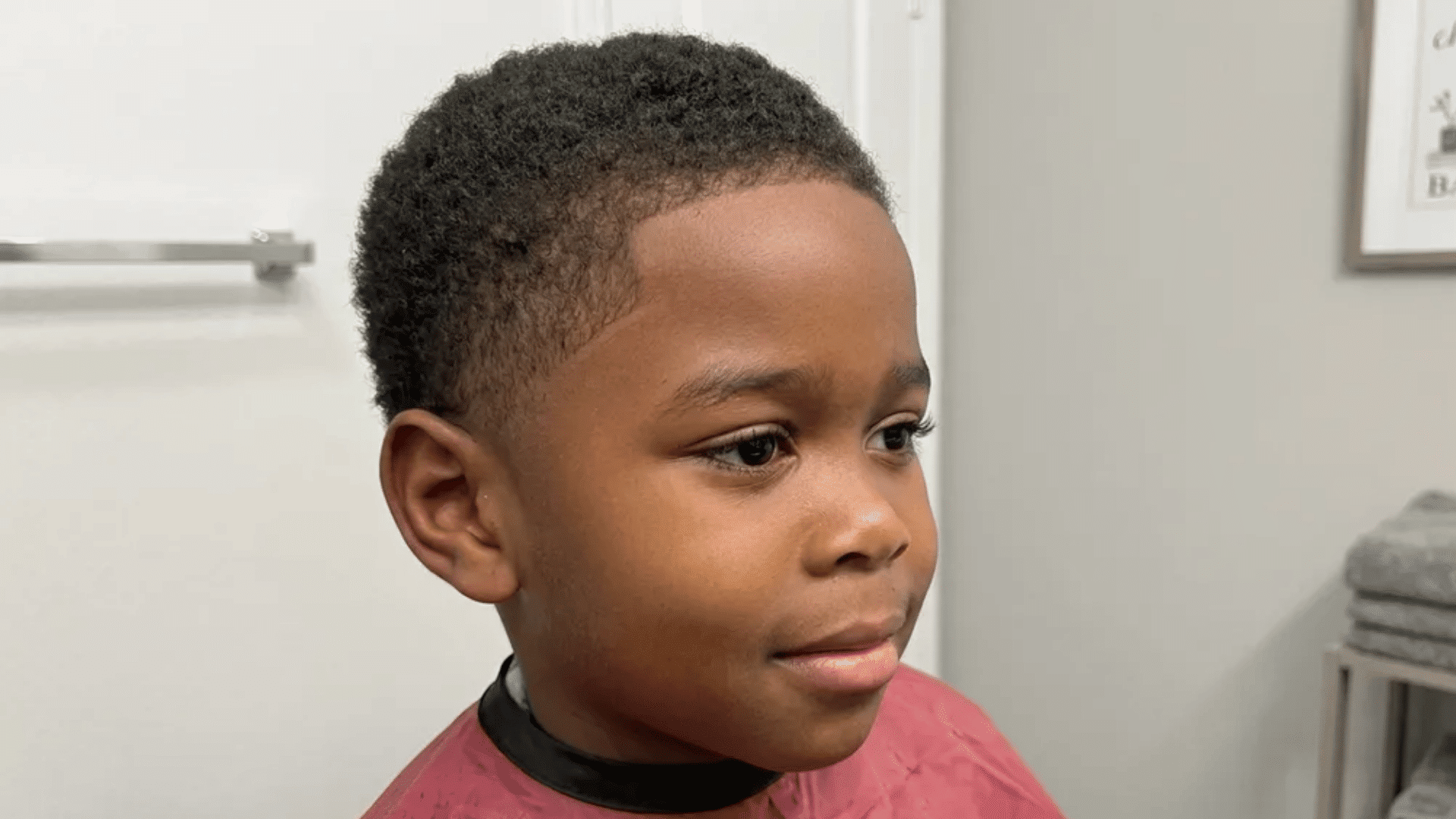 Mixed boys haircuts short curly cut with clean low fade, young boy in barber cape inside indoor barbershop setting