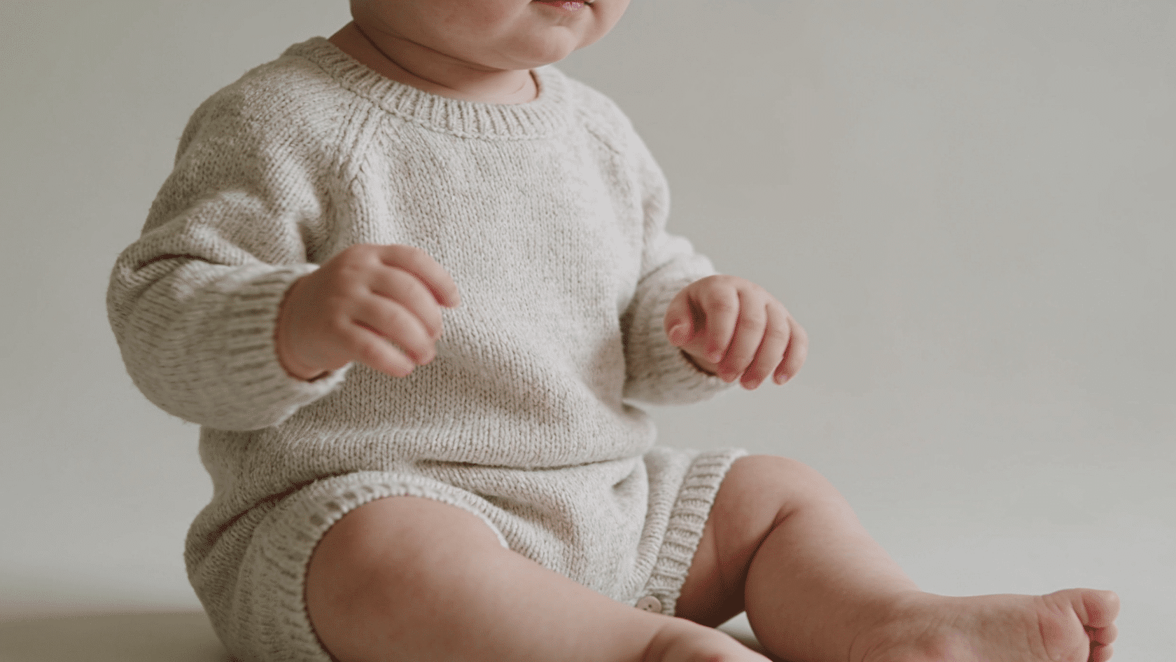 Child wearing soft cotton outfit sitting comfortably in a simple indoor newborn photoshoot setting