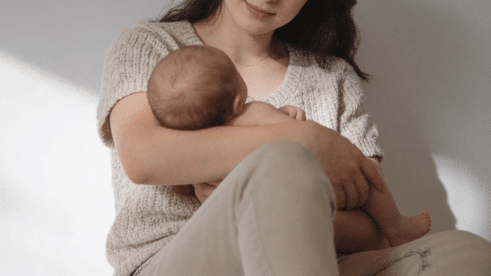 Mother wearing knit top and jeans in a simple indoor newborn photoshoot setting