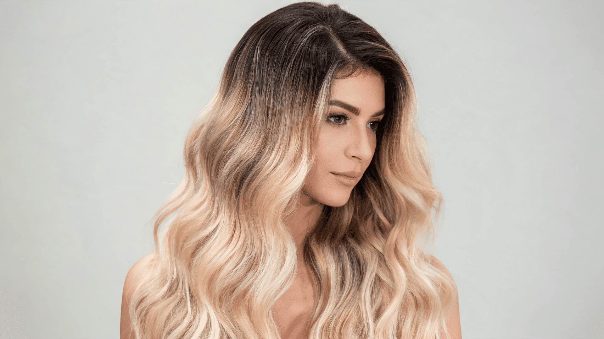Woman with a honey blonde sew-in hairstyle featuring warm golden tones and subtle dark roots.
