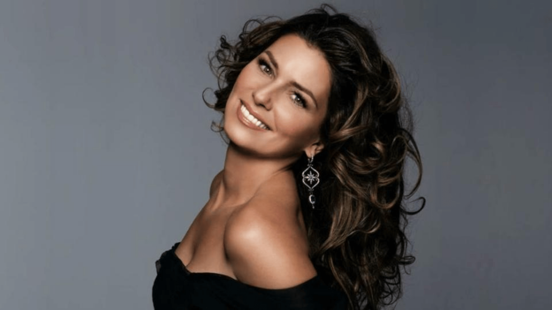 Shania Twain smiling in an elegant black outfit with statement earrings, reflecting her lifestyle