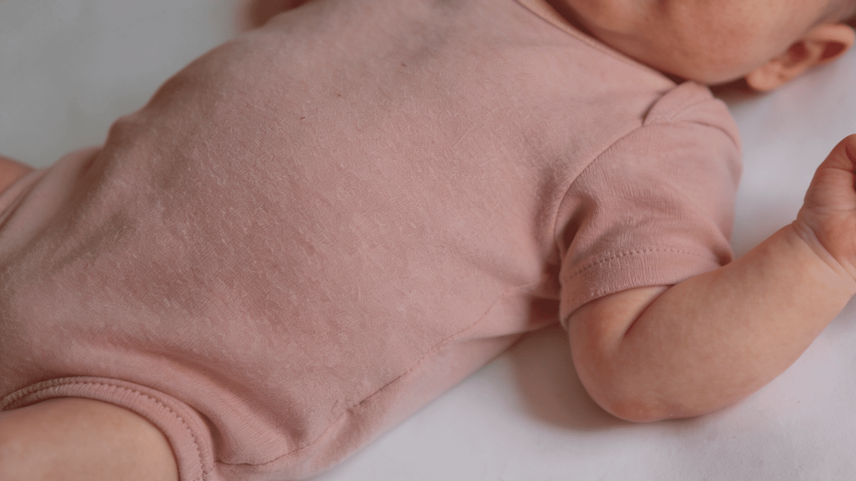 Baby wearing a plain neutral onesie in a close-up portrait against a simple background