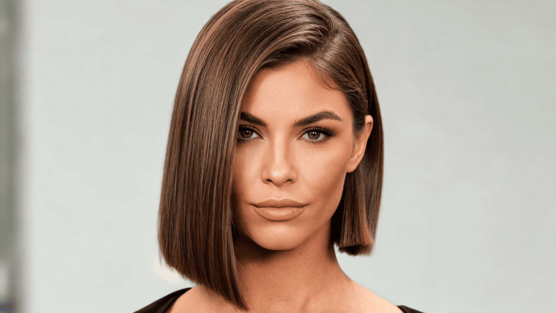 Woman with a sleek straight bob haircut featuring a side part and smooth shoulder-length layers.