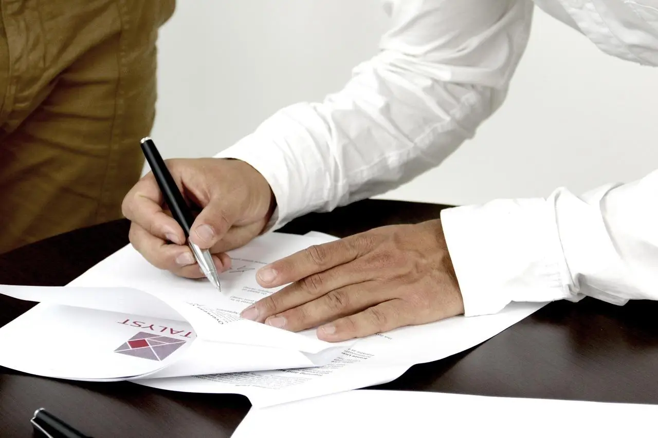 Hand signing documents on dark wooden table close up with black pen